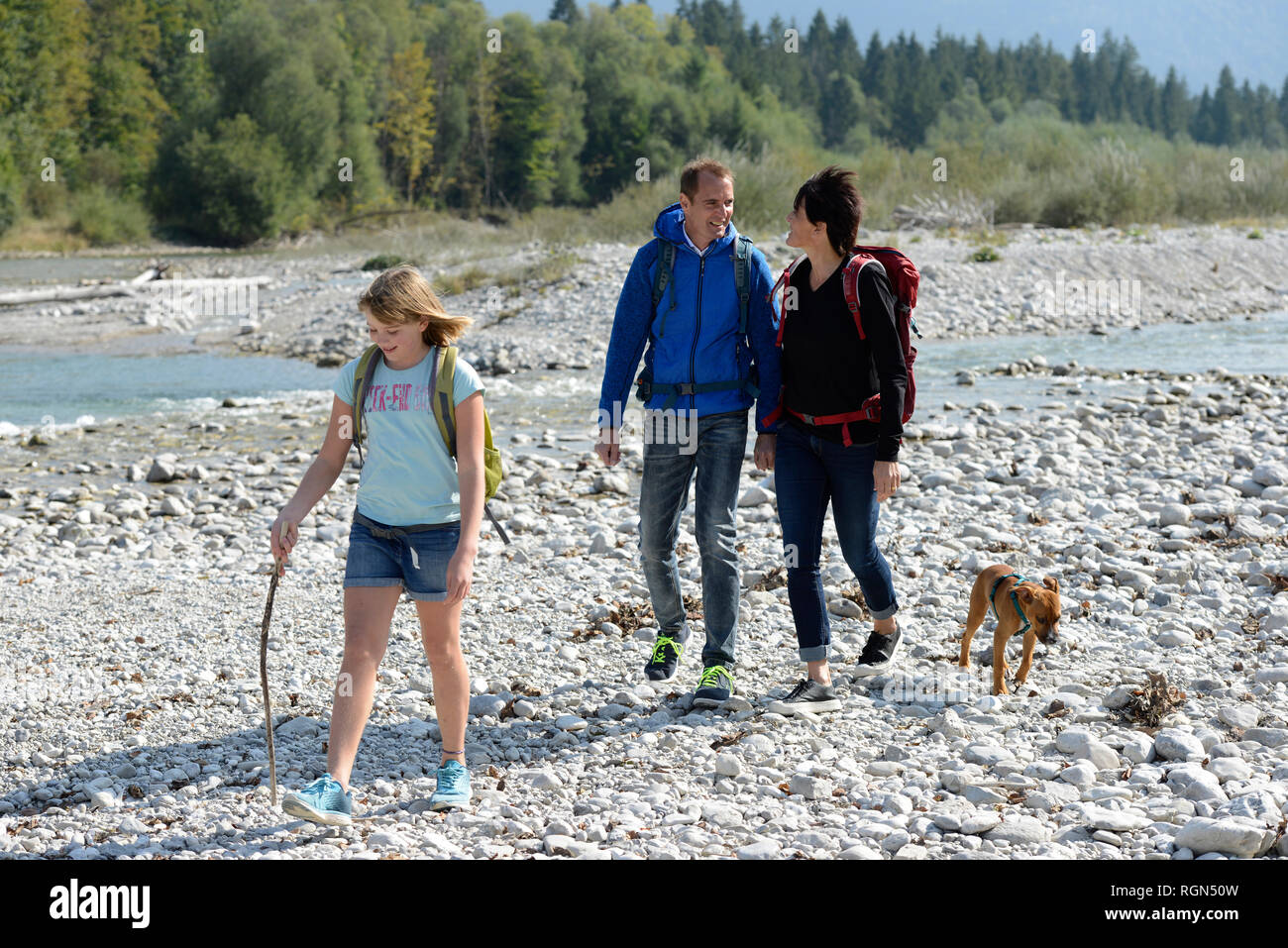 Family hiking with backpacks and a dog at the river Isar, Upper Bavaria, Germany Stock Photo