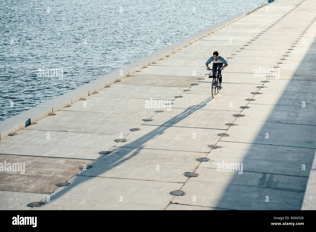 Young man riding bike on waterfront promenade at the riverside Stock Photo