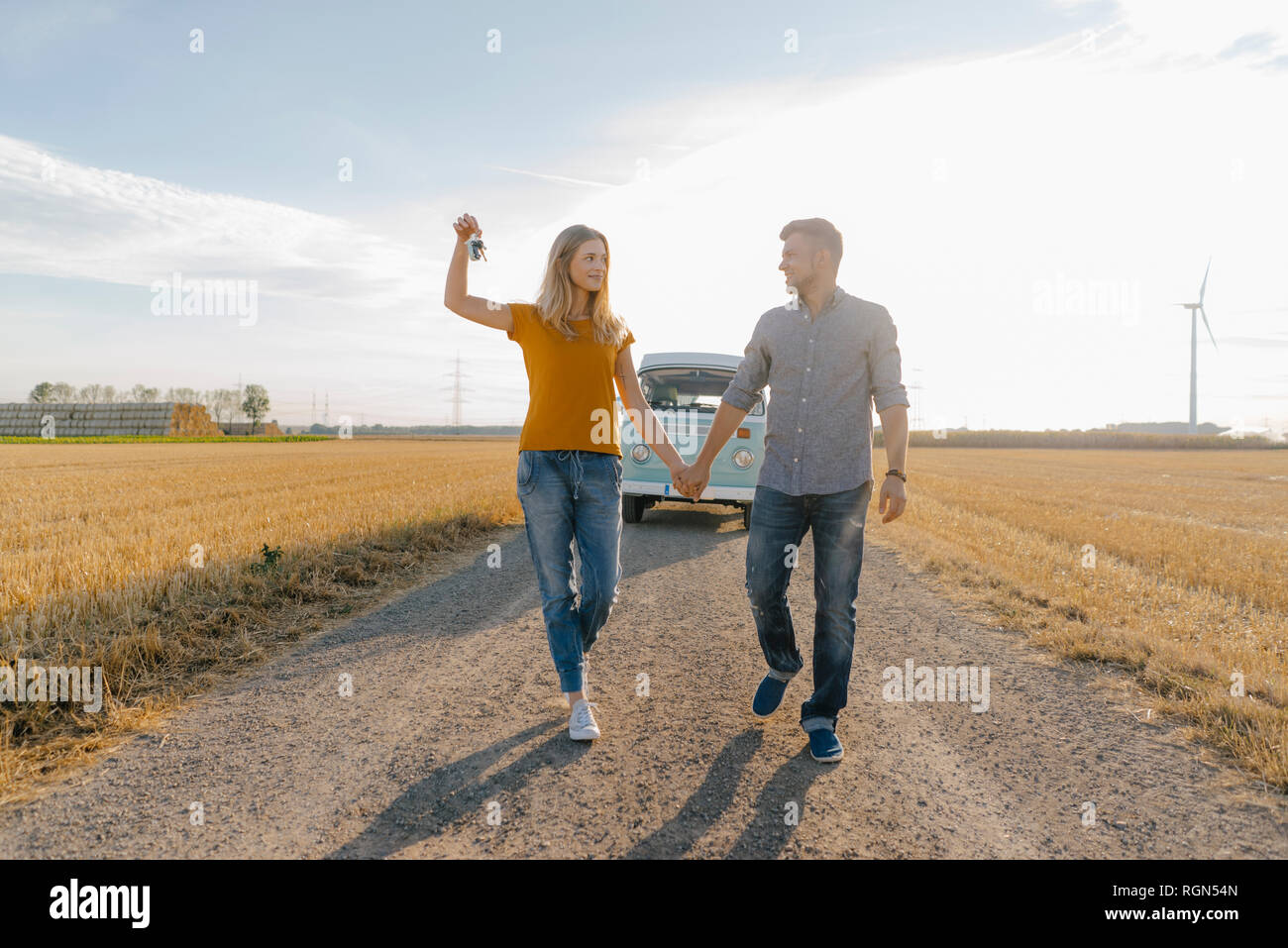 Young couple with car key walking on dirt track at camper van in rural landscape Stock Photo