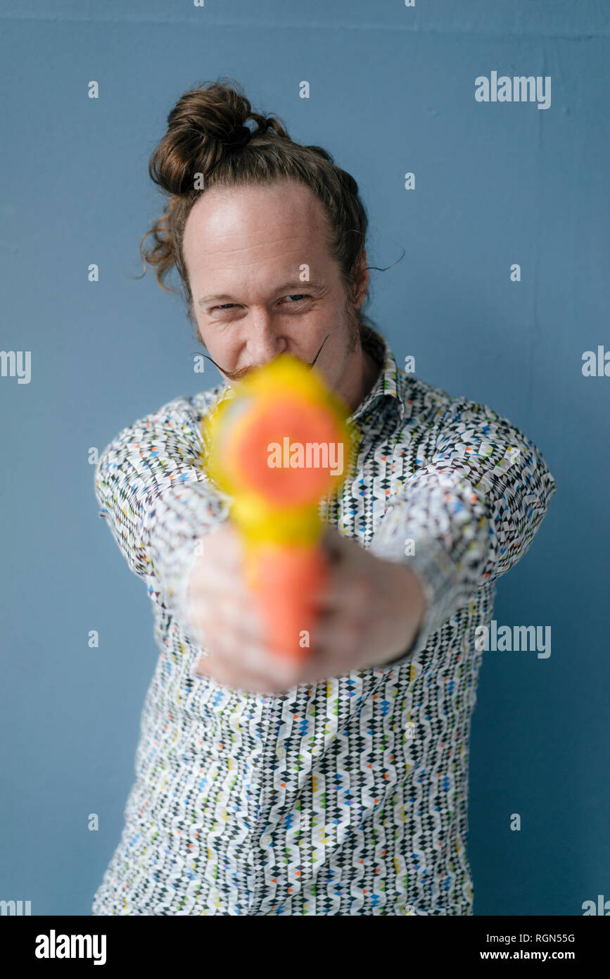 Portrait of man with moustache holding water gun at blue wall Stock Photo
