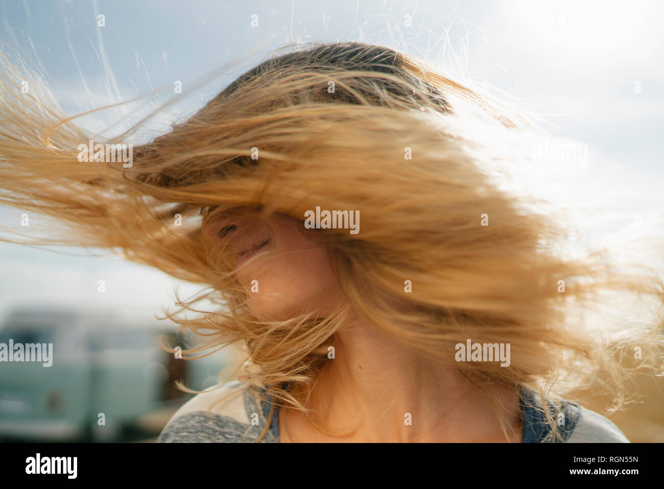 Blong young woman at camper van shaking her hair Stock Photo