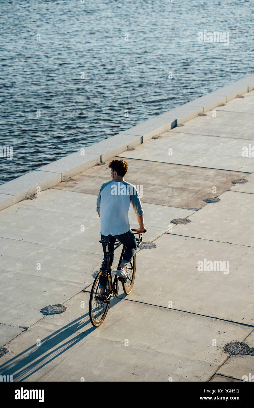 Young man riding bike on waterfront promenade at the riverside Stock Photo