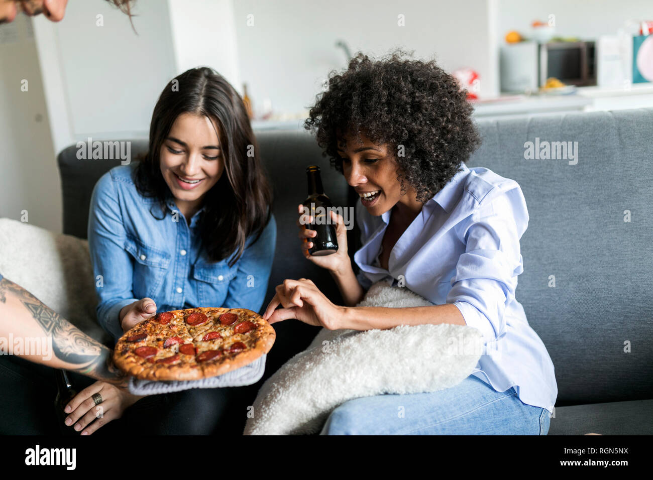 Tattooed man offering pizza to friends sitting on couch Stock Photo