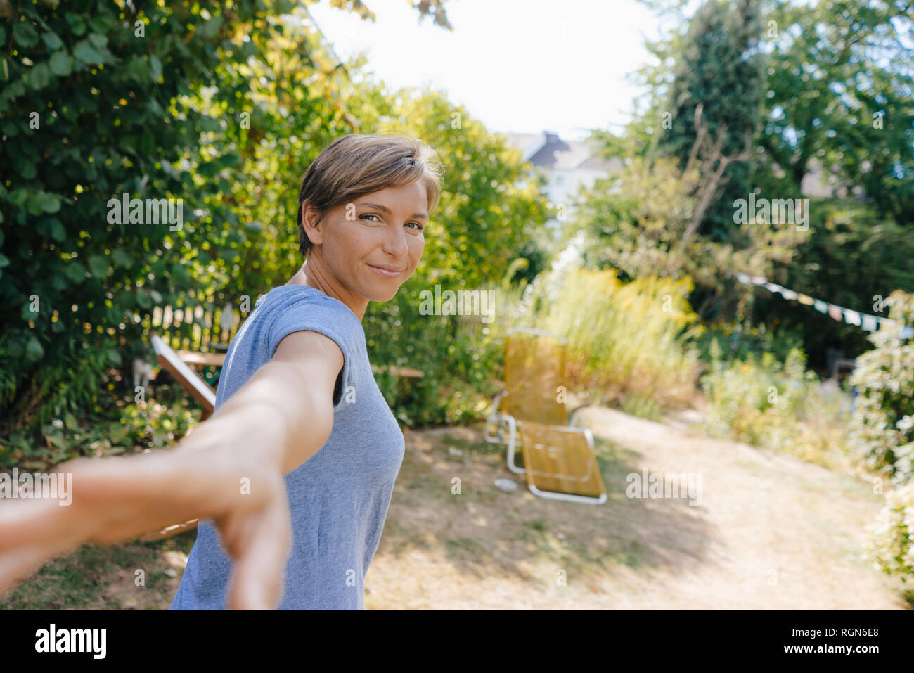 Portrait of smiling woman in garden reaching out Stock Photo