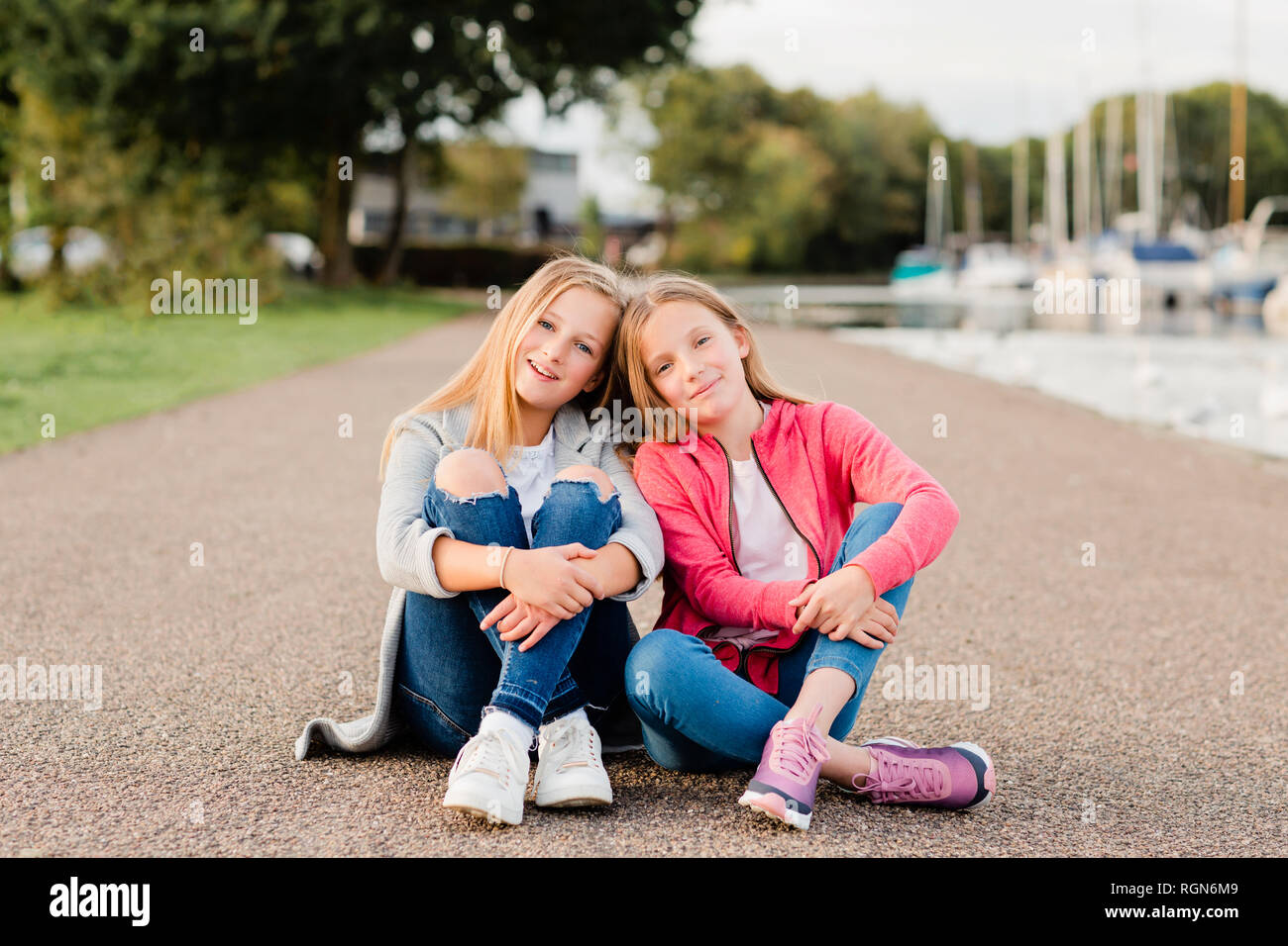 Portrait of two smiling girls sitting head to head on the ground Stock Photo