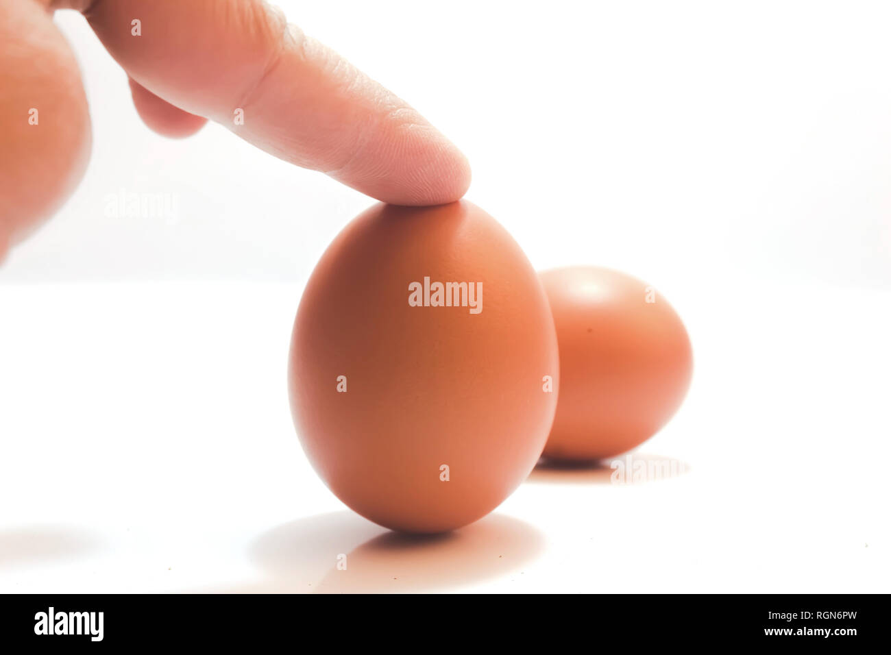 egg standing on iosalted with index finger point on top of egg white background Stock Photo