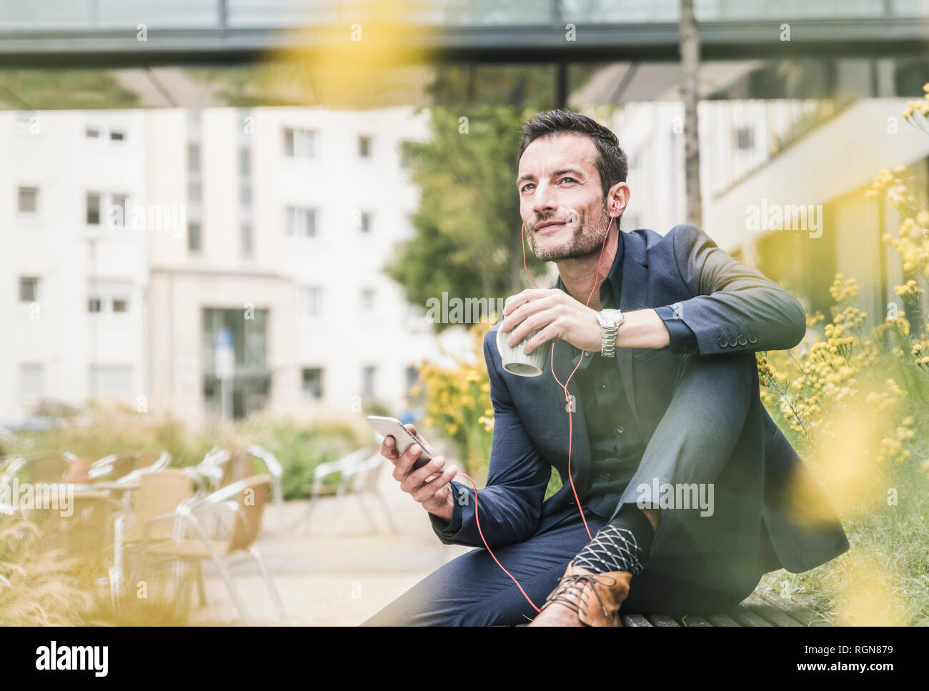 Businessman sitting outside, taking a break, listening music from his smartphone, drinking coffee Stock Photo