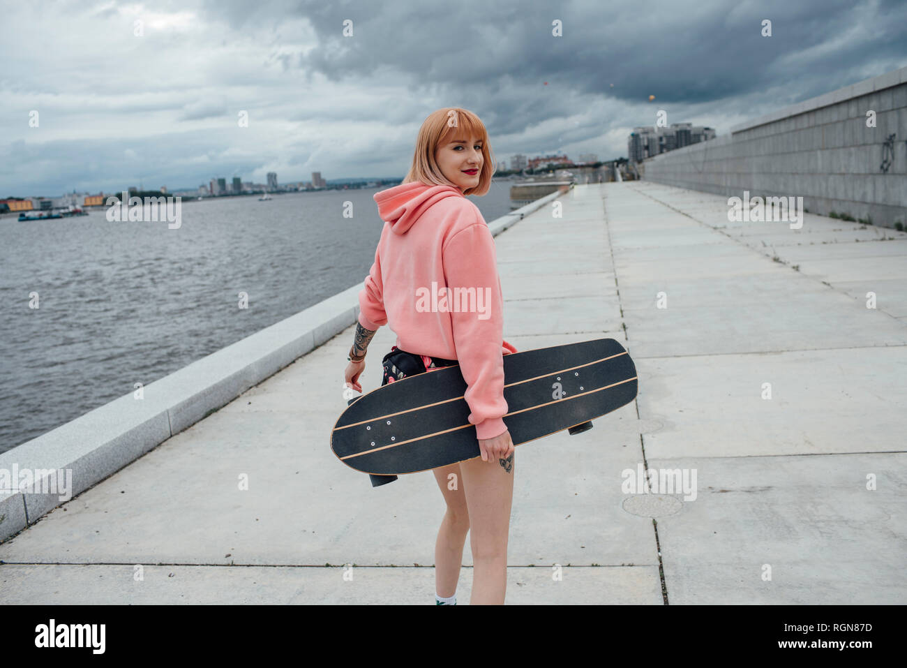 Young woman holding skateboard walking at the riverside Stock Photo