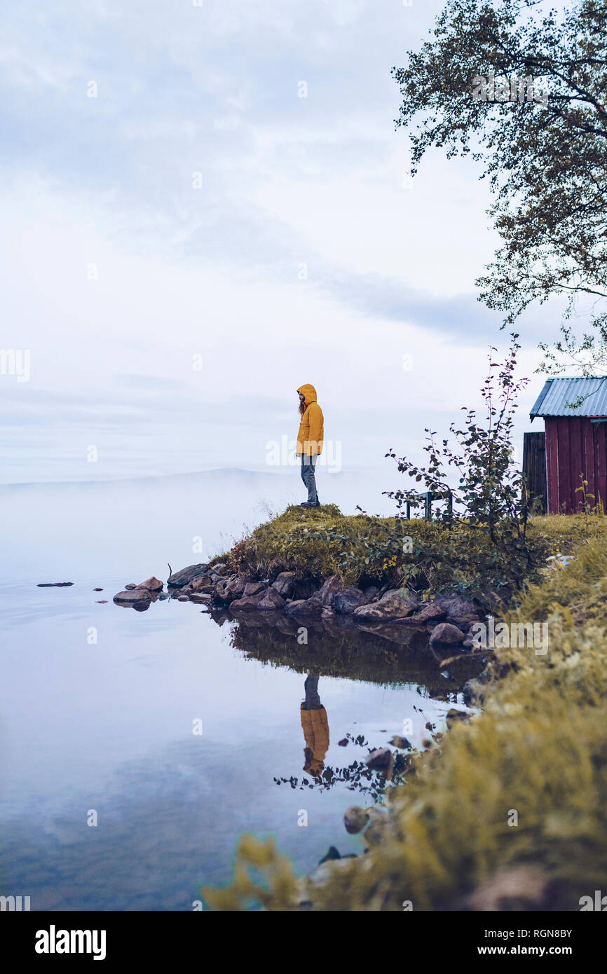 Sweden, Lapland, man wearing  windbreaker standing at water's edge looking at distance Stock Photo