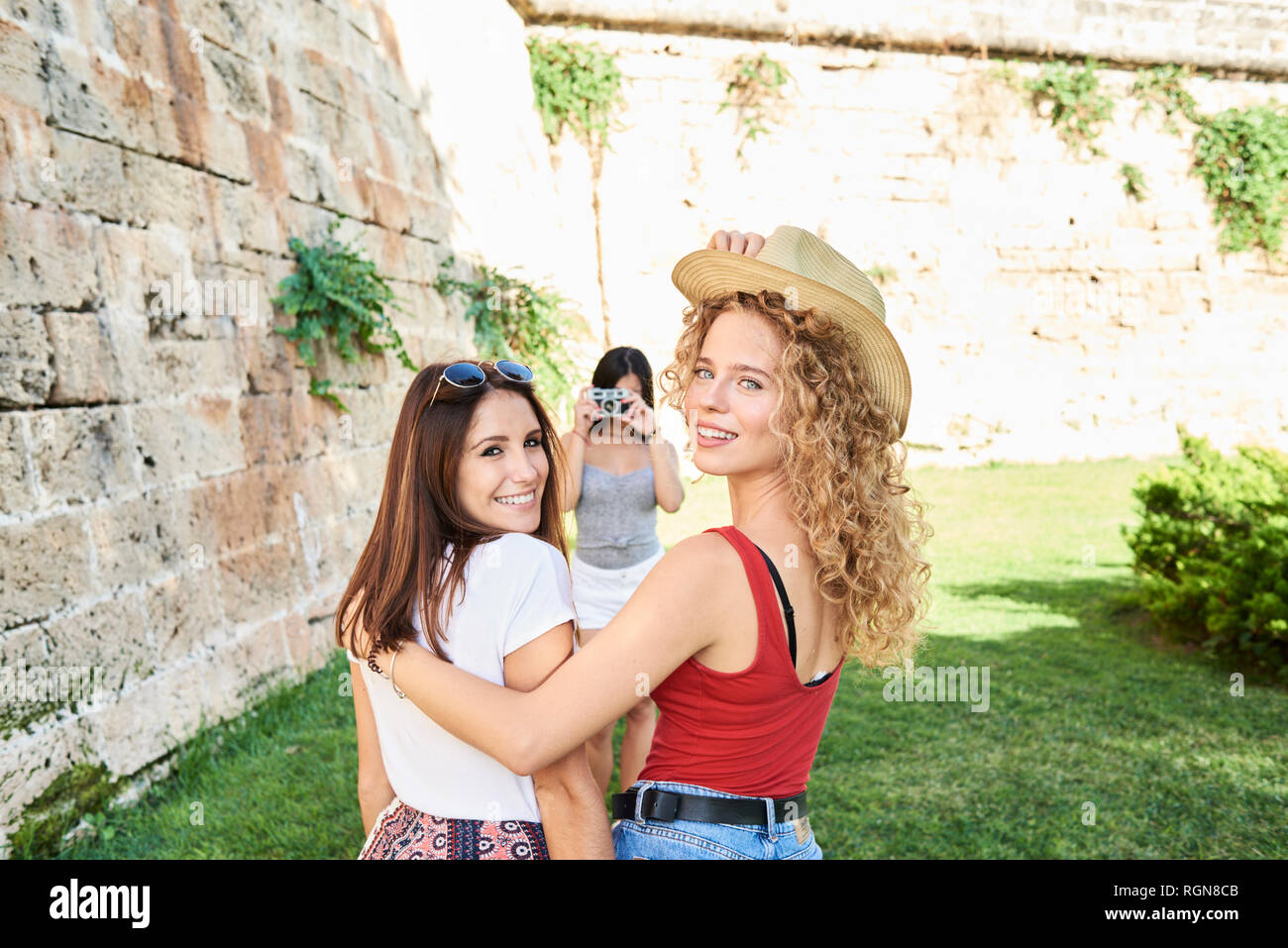 Spain, Mallorca, Palma, two female friends smiling at camera while another friend is taking a picture of them Stock Photo