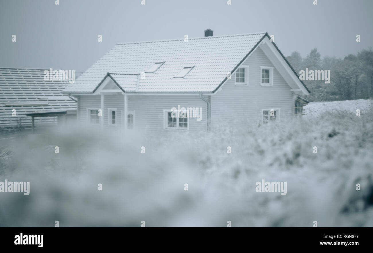 Grass and snow, frame house in the background Stock Photo