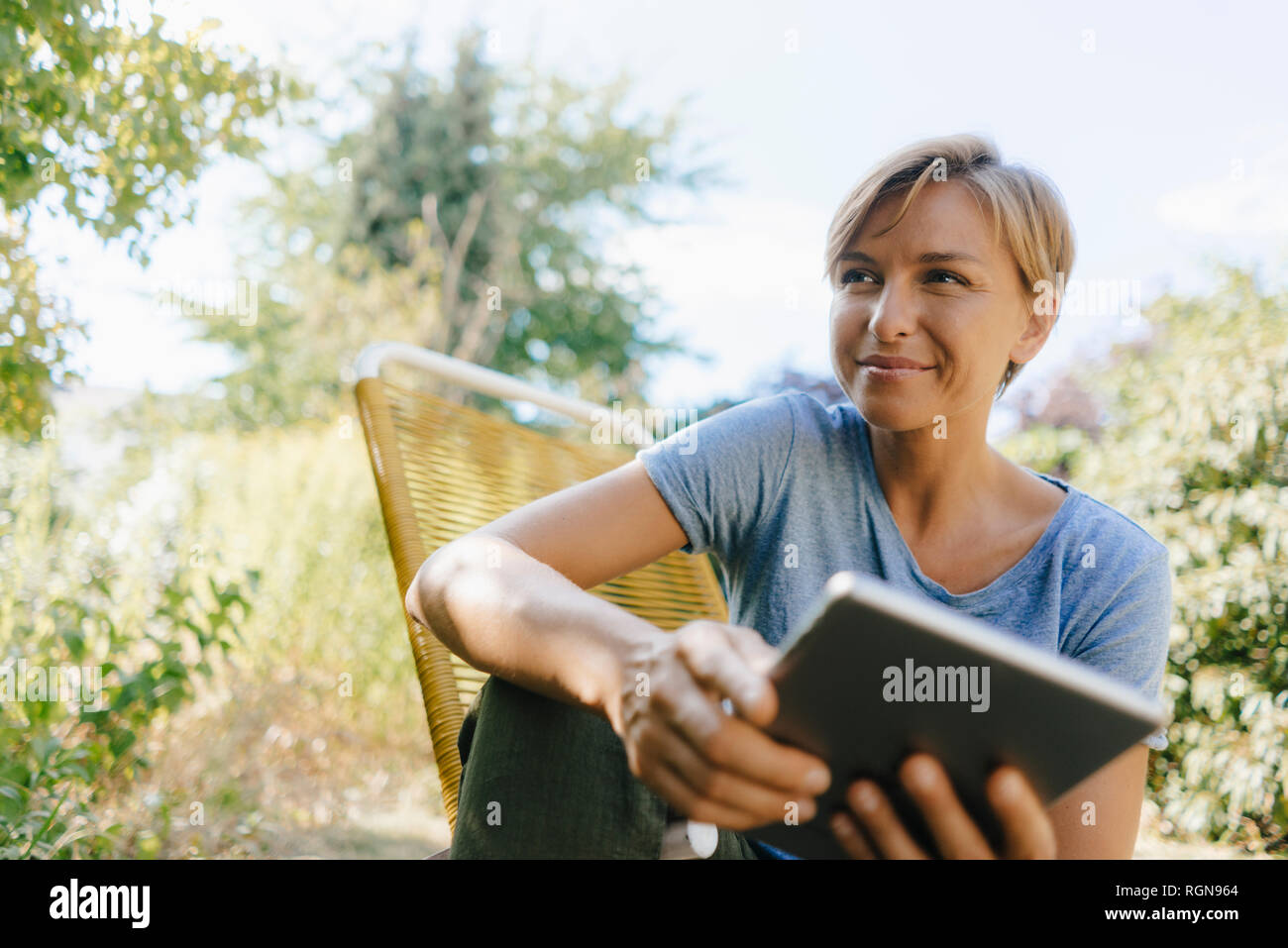 Woman sitting in garden on chair holding tablet Stock Photo