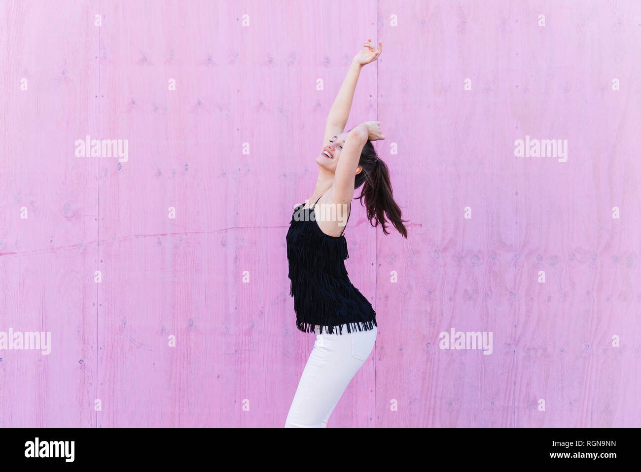 Happy young woman standing in front of pink wall Stock Photo - Alamy