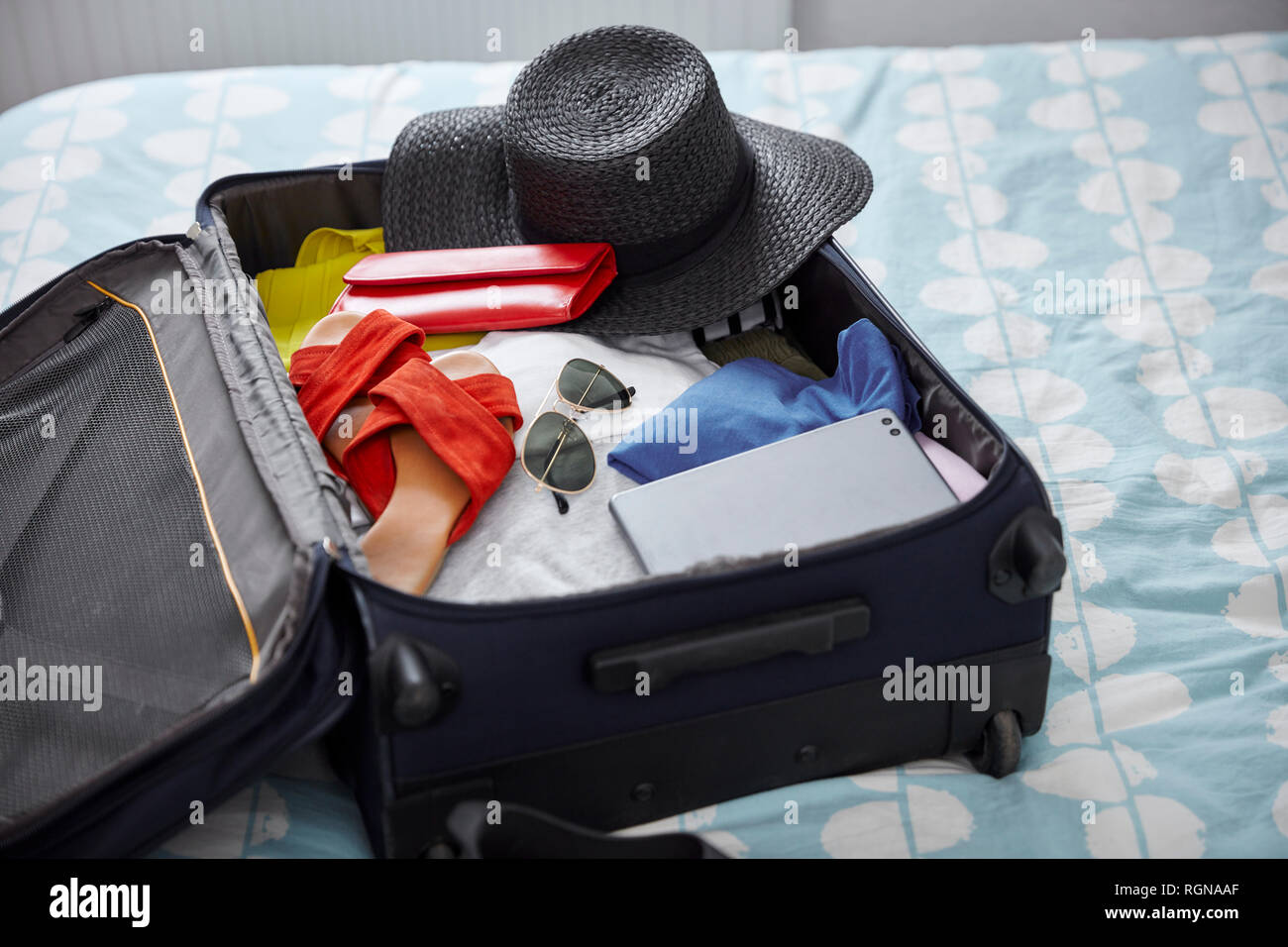 Suitcase with summer vacation utensils on bed Stock Photo