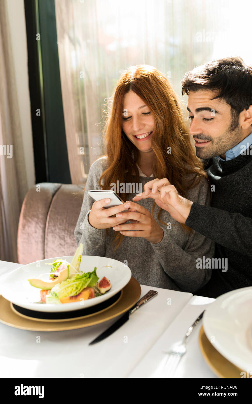 Happy couple using cell phone in a restaurant Stock Photo