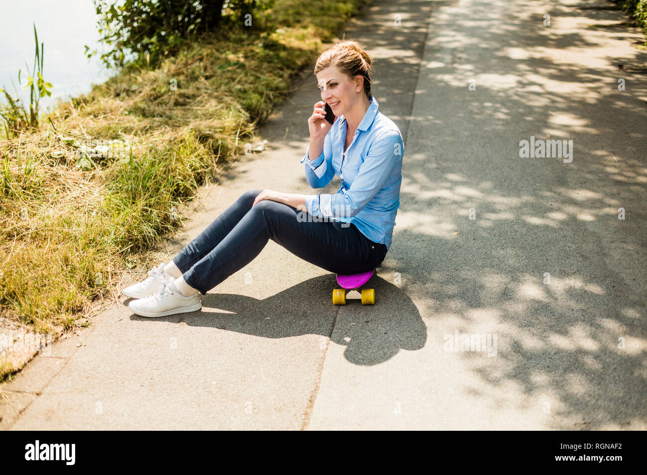 Smiling woman sitting on penny board talking on cell phone Stock Photo