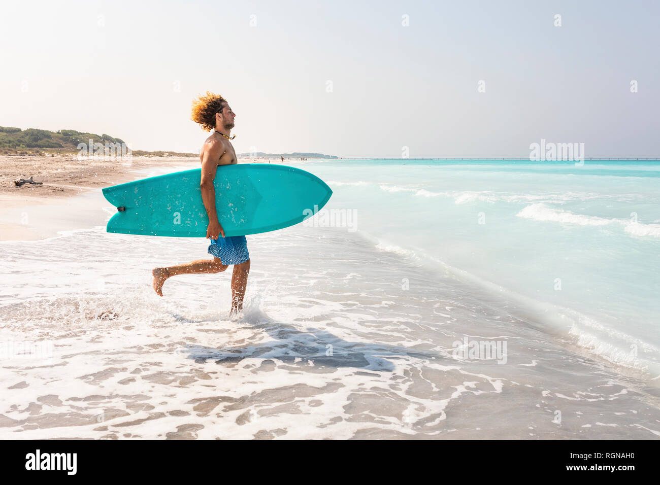 Young man running into ghe sea, carrying his surfboard Stock Photo
