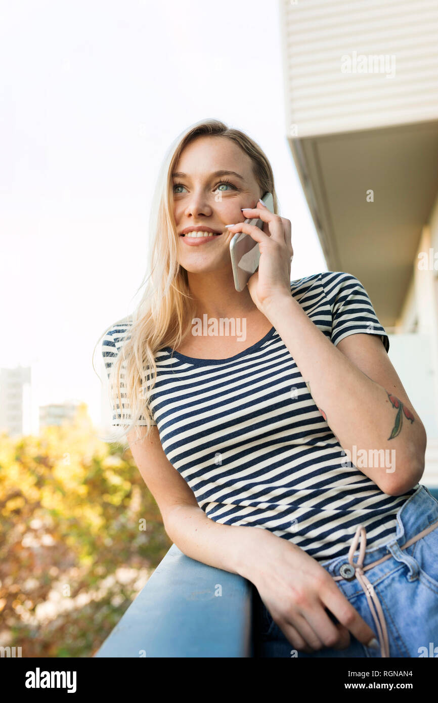 Smiling young woman talking on cell phone on balcony Stock Photo