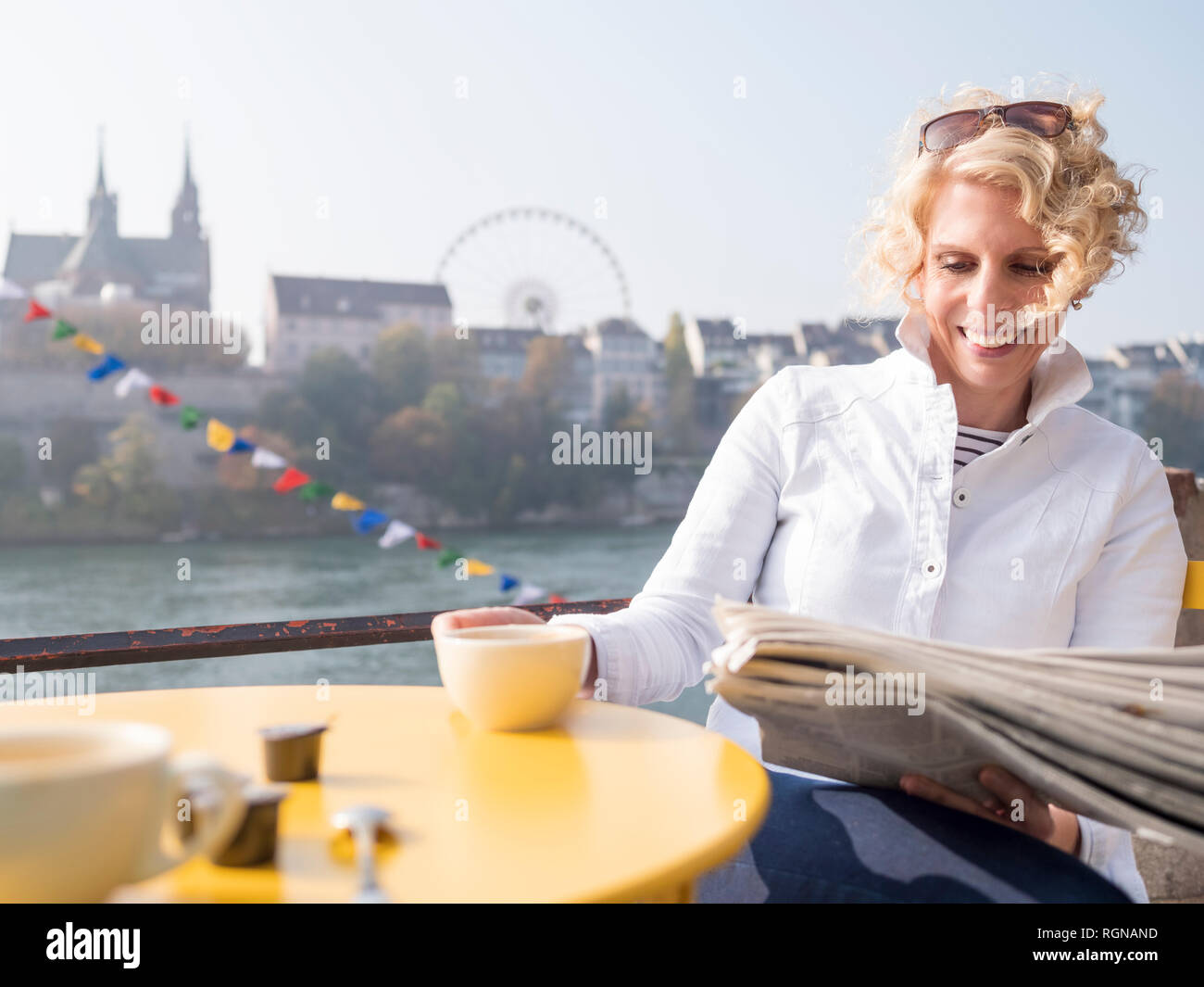 Switzerland, Basel, smiling woman reading newspaper in a street cafe at River Rhine Stock Photo