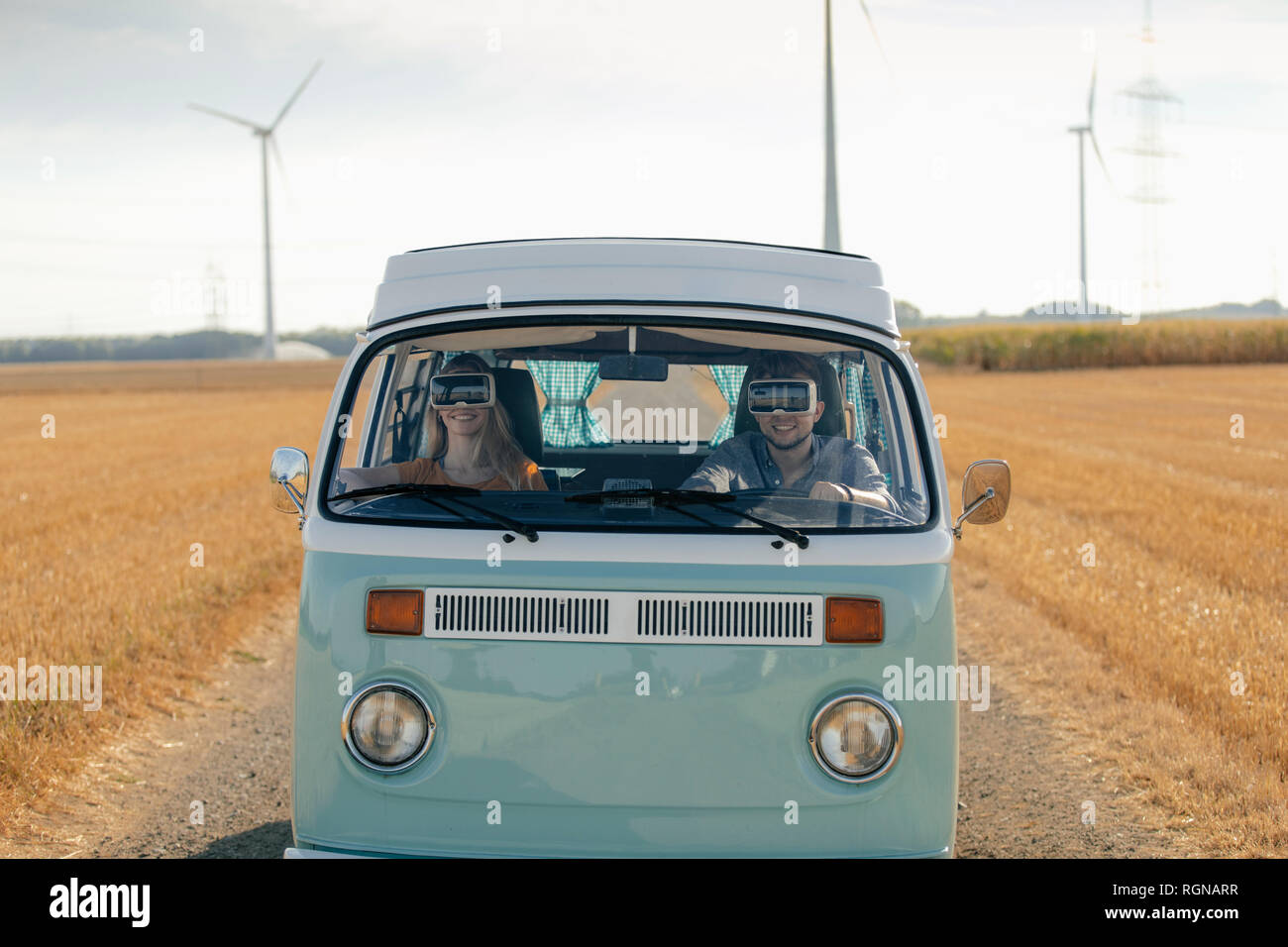 Smiling couple wearing VR glasses driving camper van in rural landscape Stock Photo