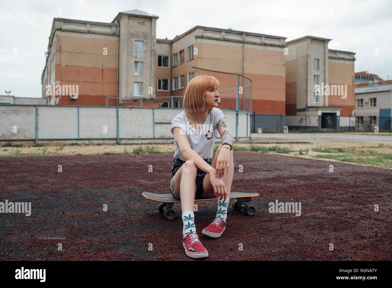 Cool young woman sitting on carver skateboard outdoors Stock Photo