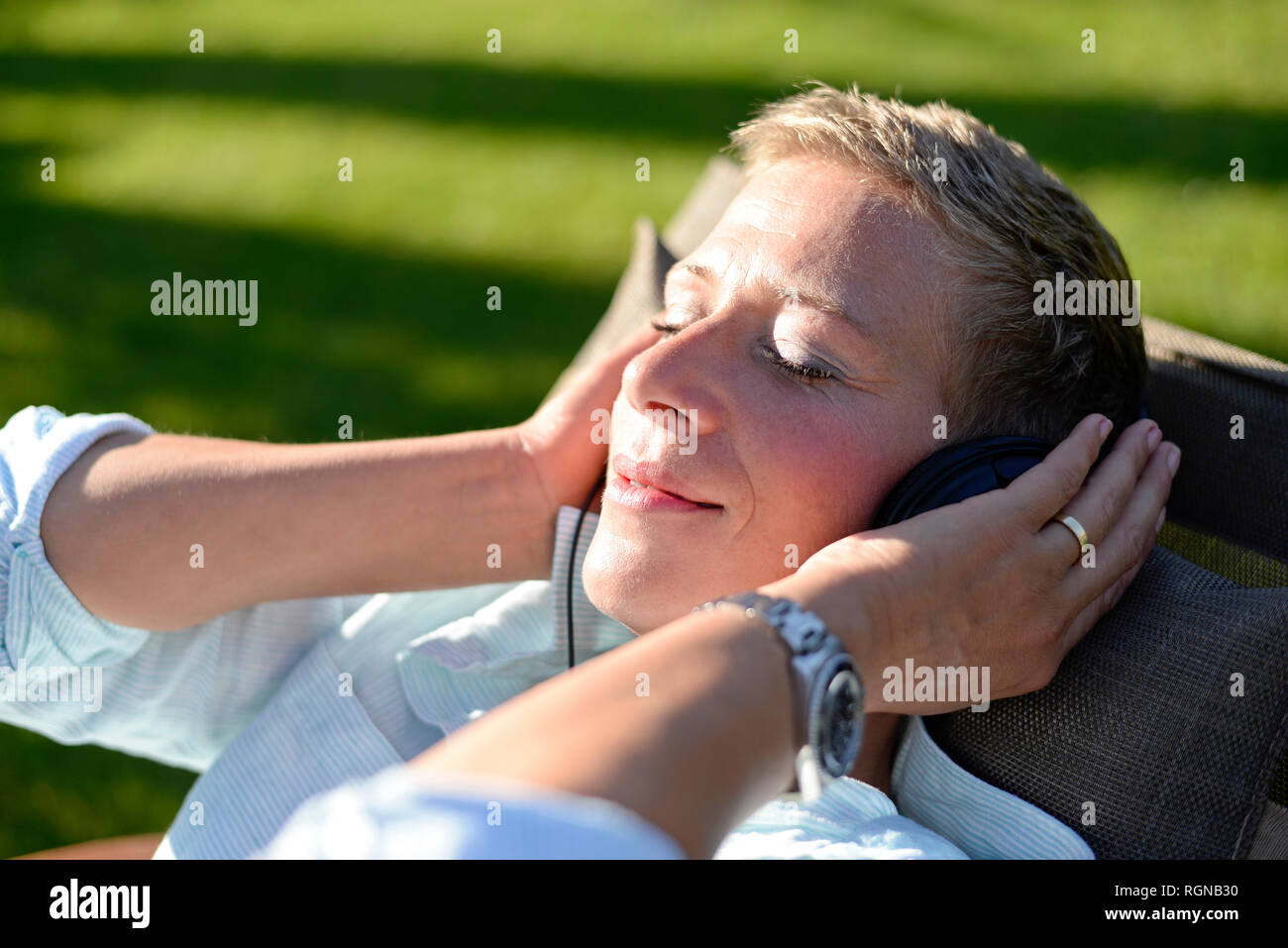 Portrait of woman listening music with headphones in the garden Stock Photo