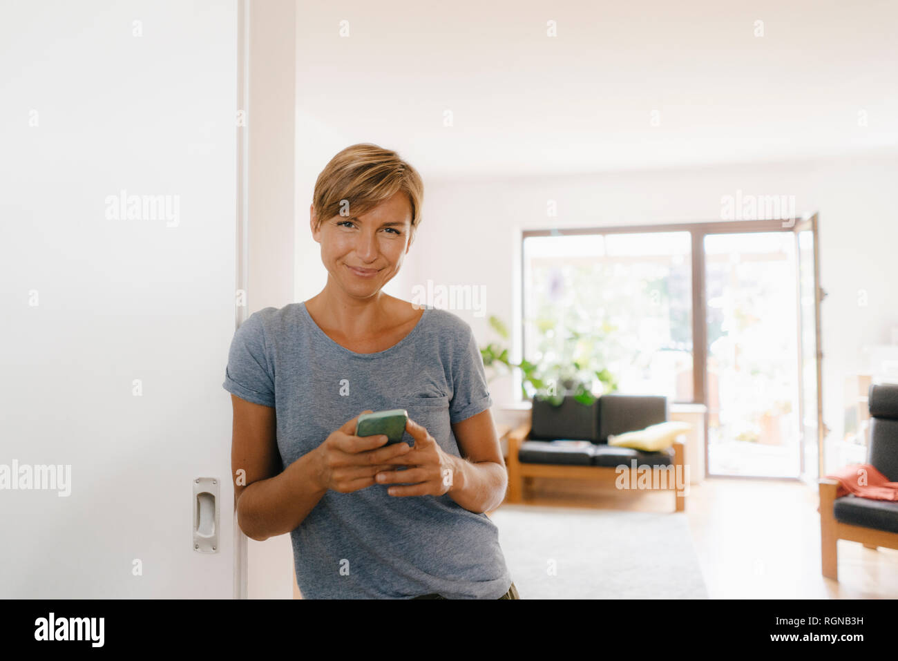 Portrait of smiling woman at home holding cell phone Stock Photo