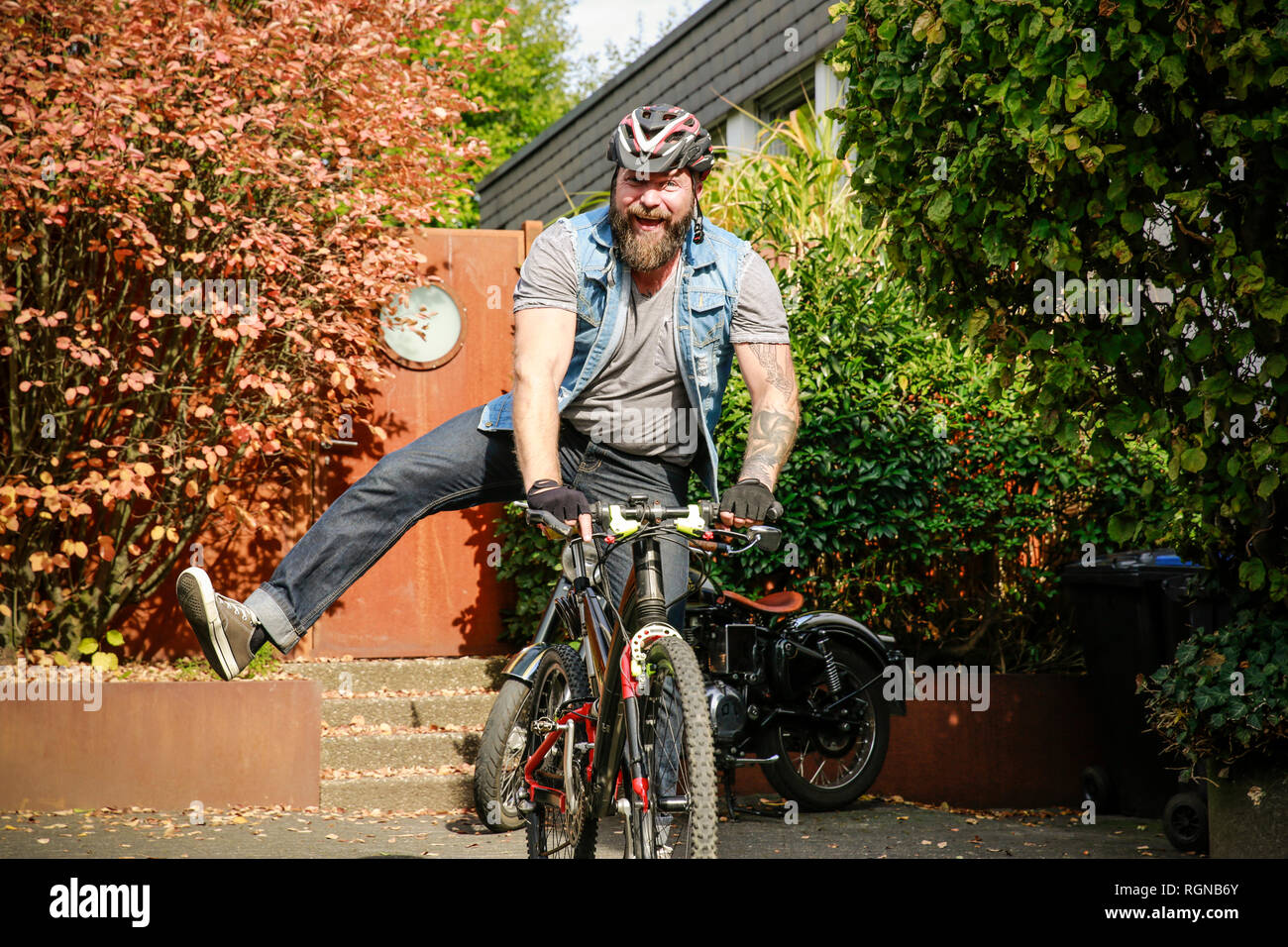 Portrait of happy man switching from motorbike to bicycle Stock Photo