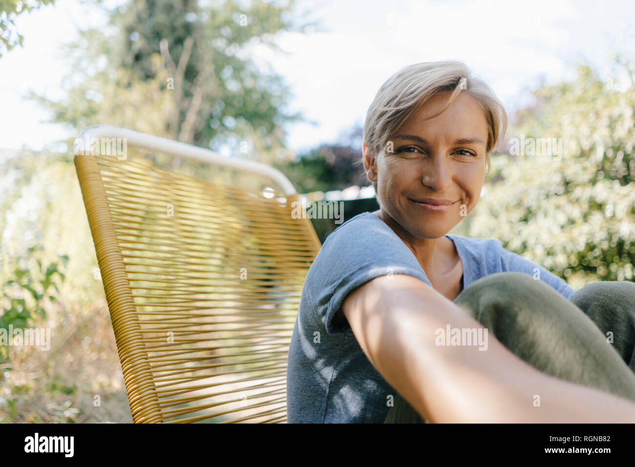 Portrait of smiling woman sitting in garden on chair Stock Photo