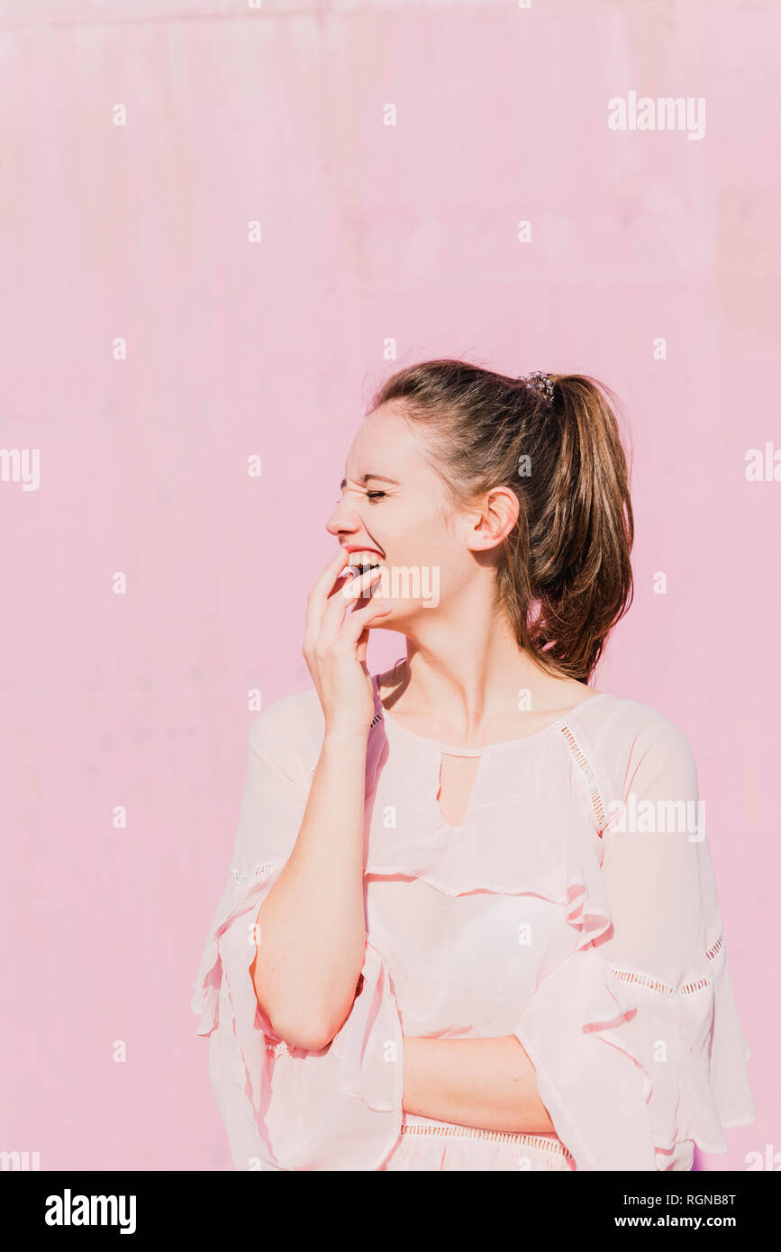 Laughing young woman in front of pink wall Stock Photo