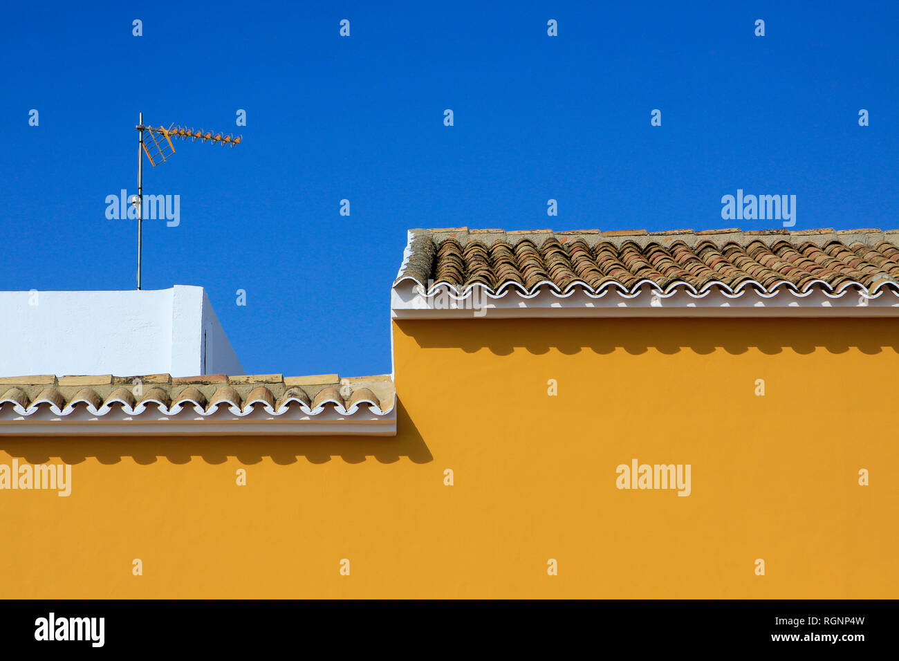 Mediterranean ochre wall and traditional rooftop tiles with brilliant blue sky, Oliva, Valencia, Spain Stock Photo