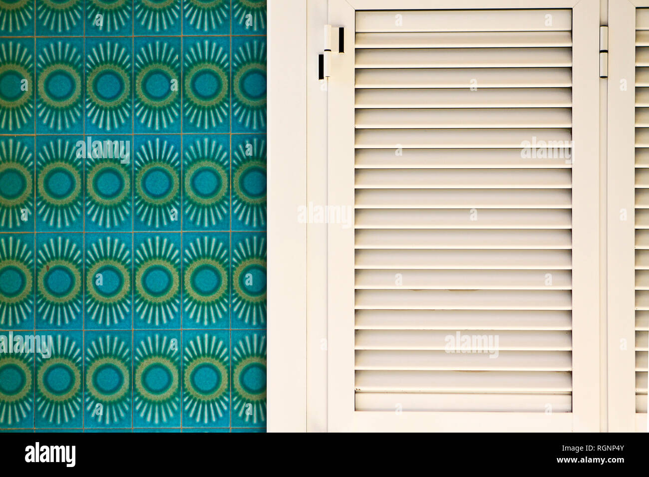 Traditional turquoise and green Spanish tiles on wall with white window shutters in Oliva, Valencia, Spain Stock Photo