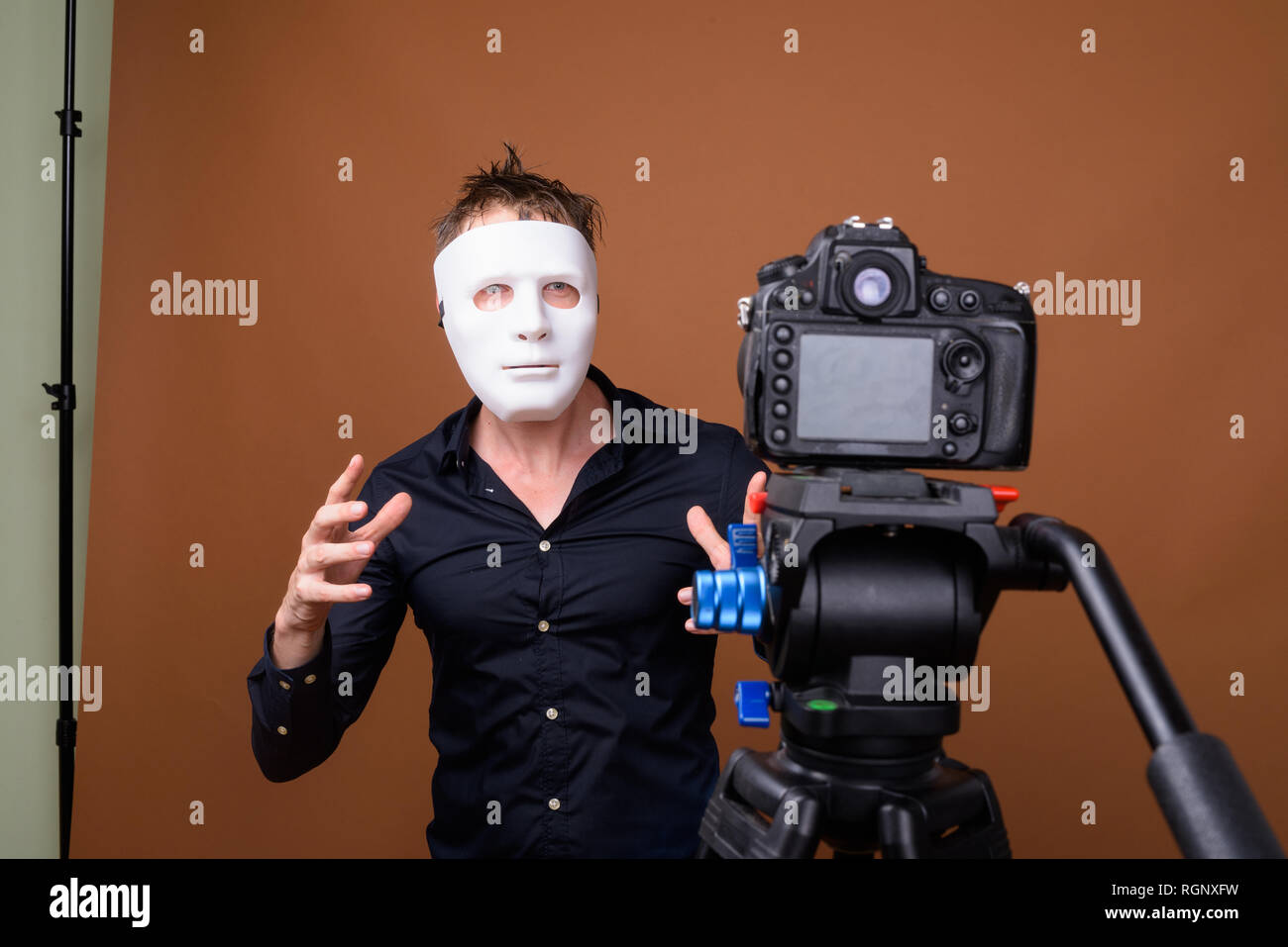 Young man influencer wearing mask while vlogging with camera in studio Stock Photo