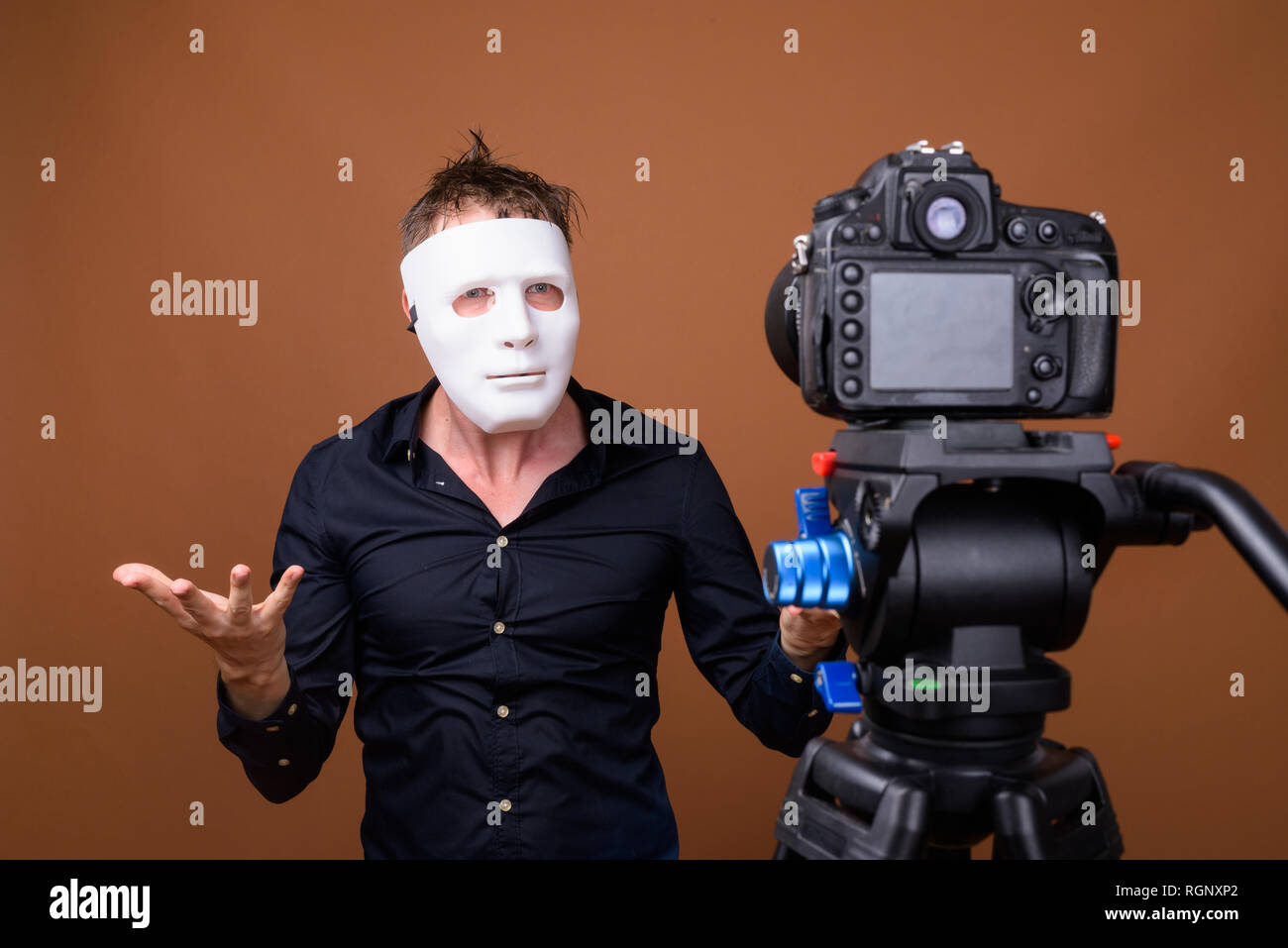 Young man influencer wearing mask while vlogging with camera in studio Stock Photo