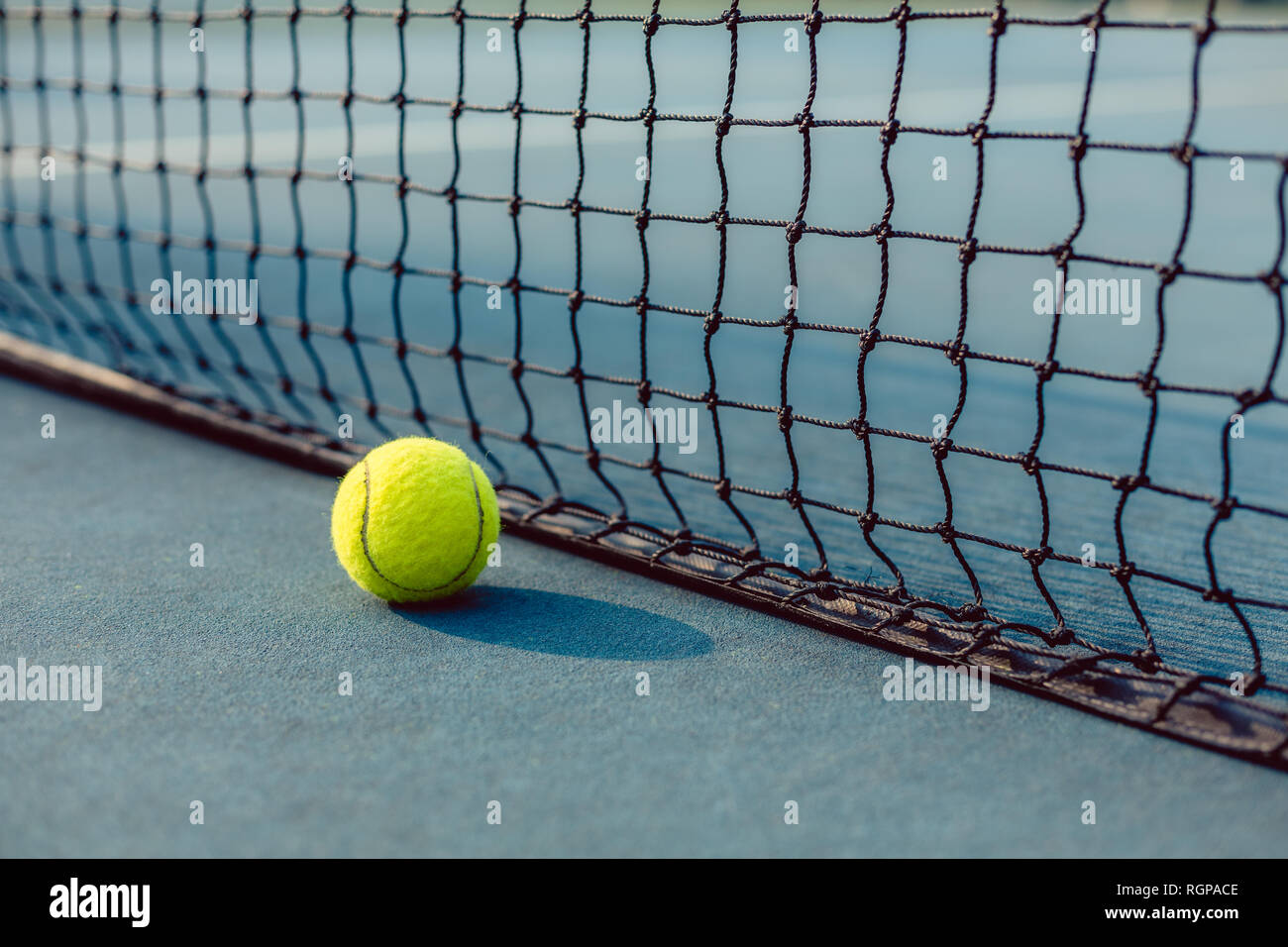 Close-up of a fluorescent yellow ball in front of the net of a tennis court Stock Photo