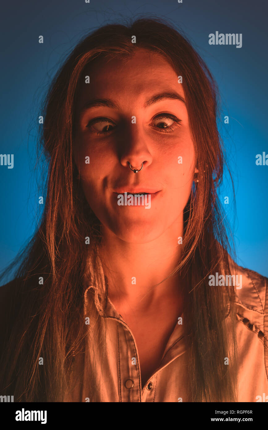 Young lady with piercing doing funny faces in redness on blue background Stock Photo