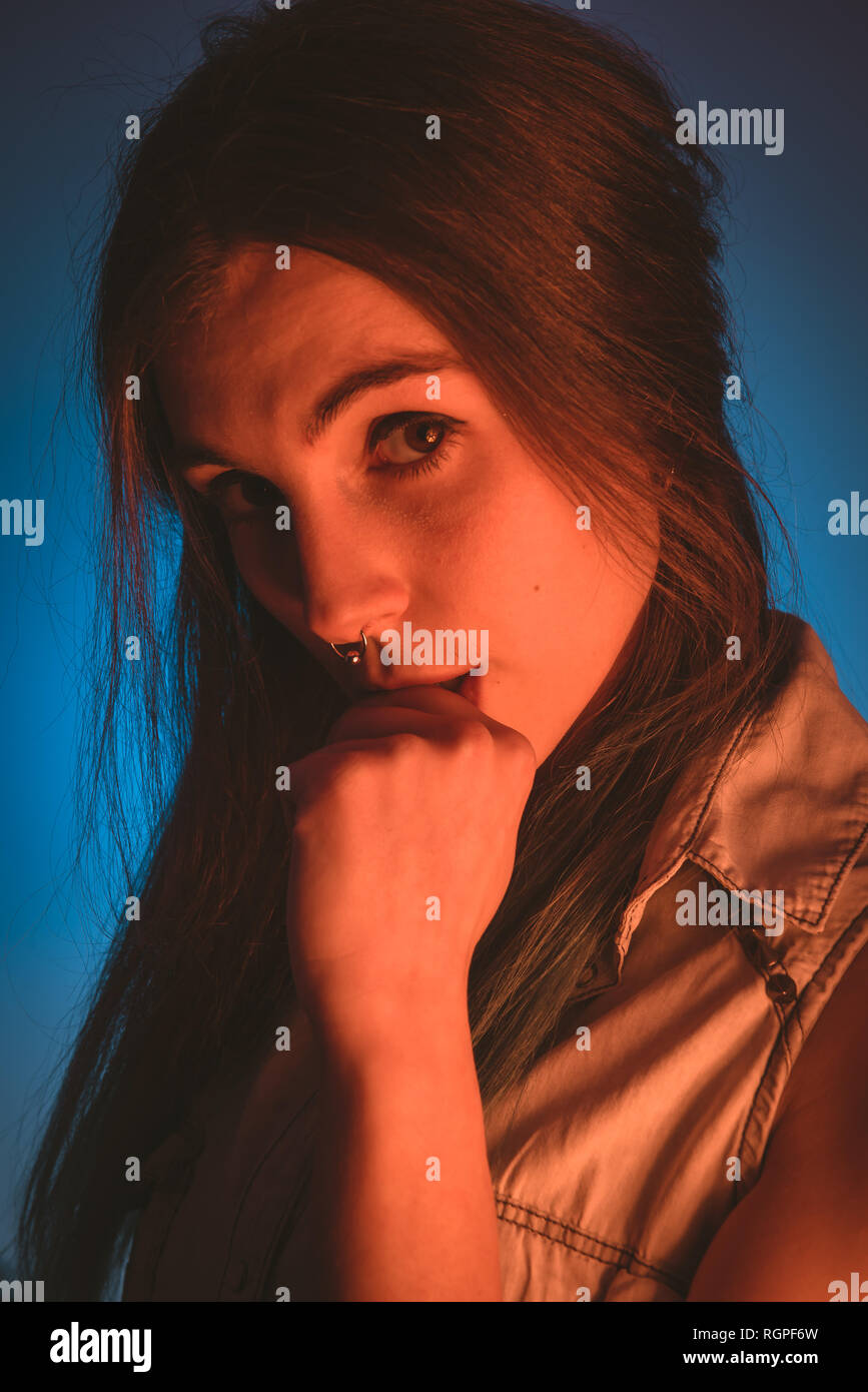 Charming young lady with piercing and fist near mouth looking at camera in redness on blue background Stock Photo