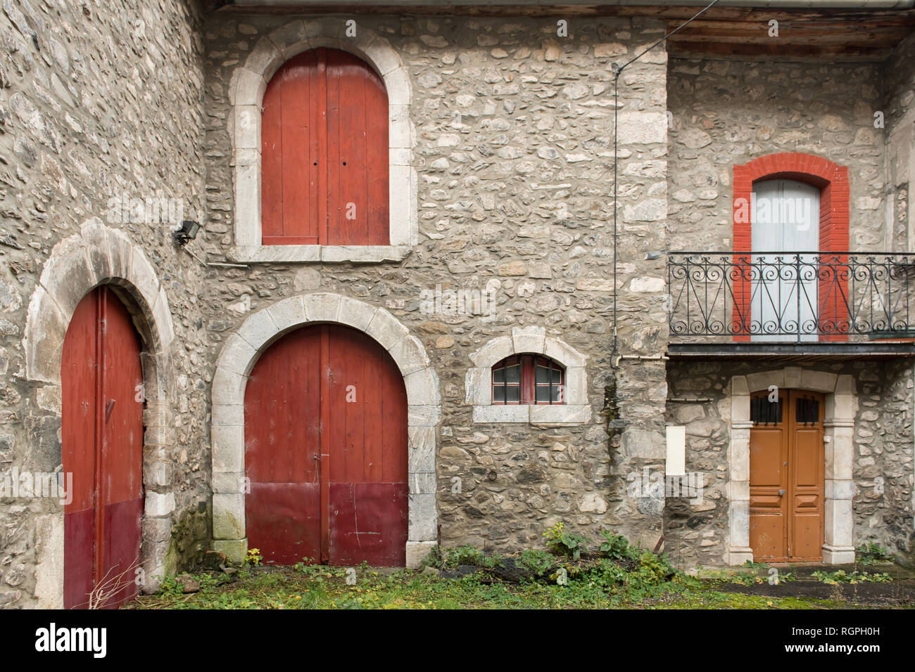 Yard With Green Grass Between Grey Rock Old House With Red Doors