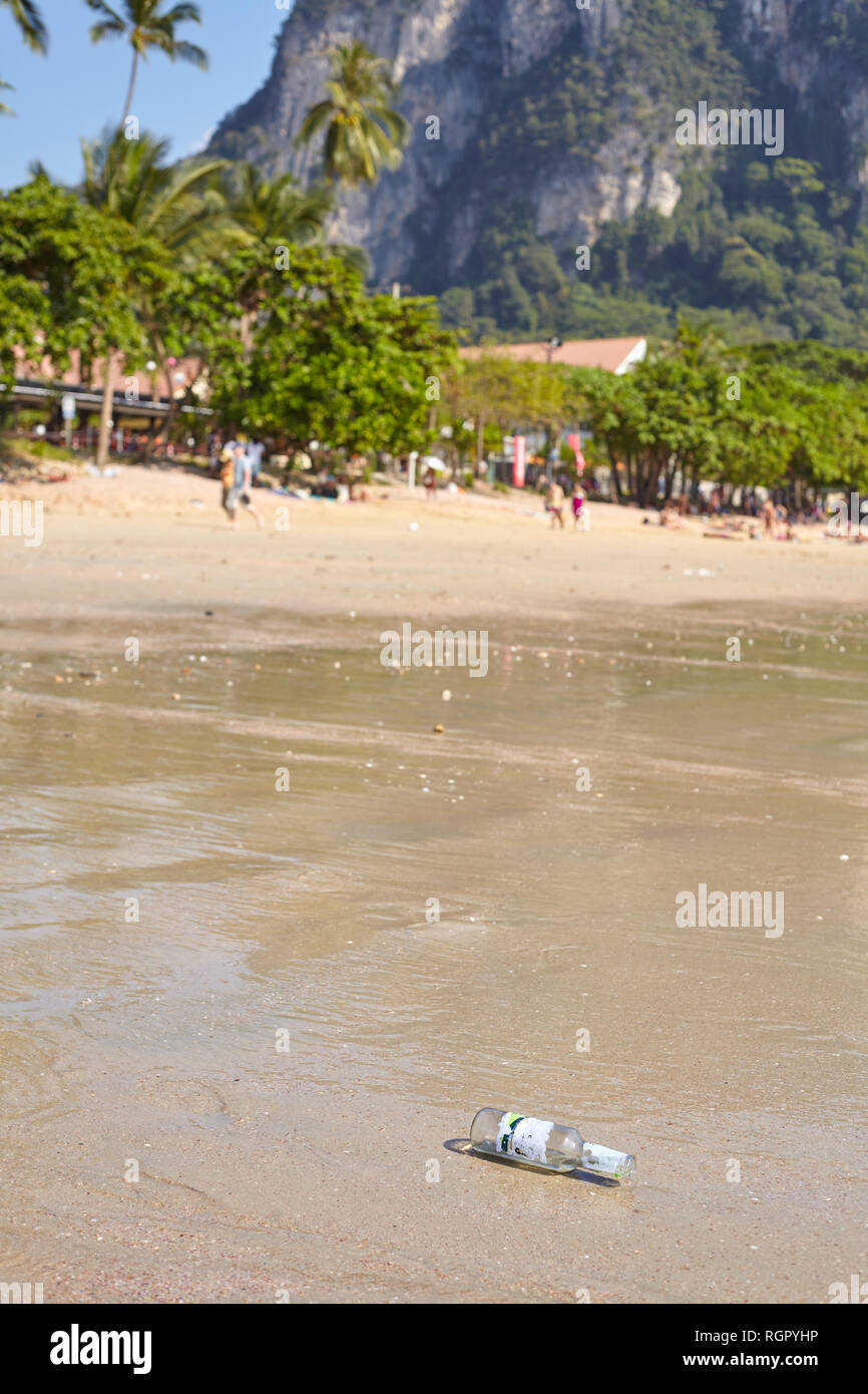 Empty glass bottle left on a beach, tourism development related environment littering concept, Thailand. Stock Photo