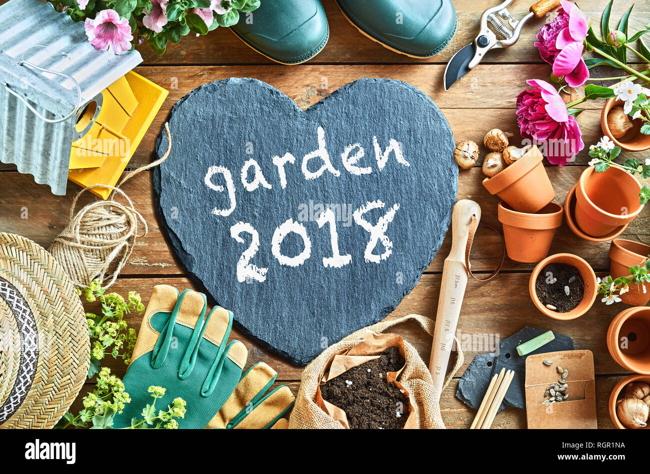 Garden season 2018 concept overhead photo of gardening equipment arranged on the floor, with grey heart-shaped board with white inscription Stock Photo