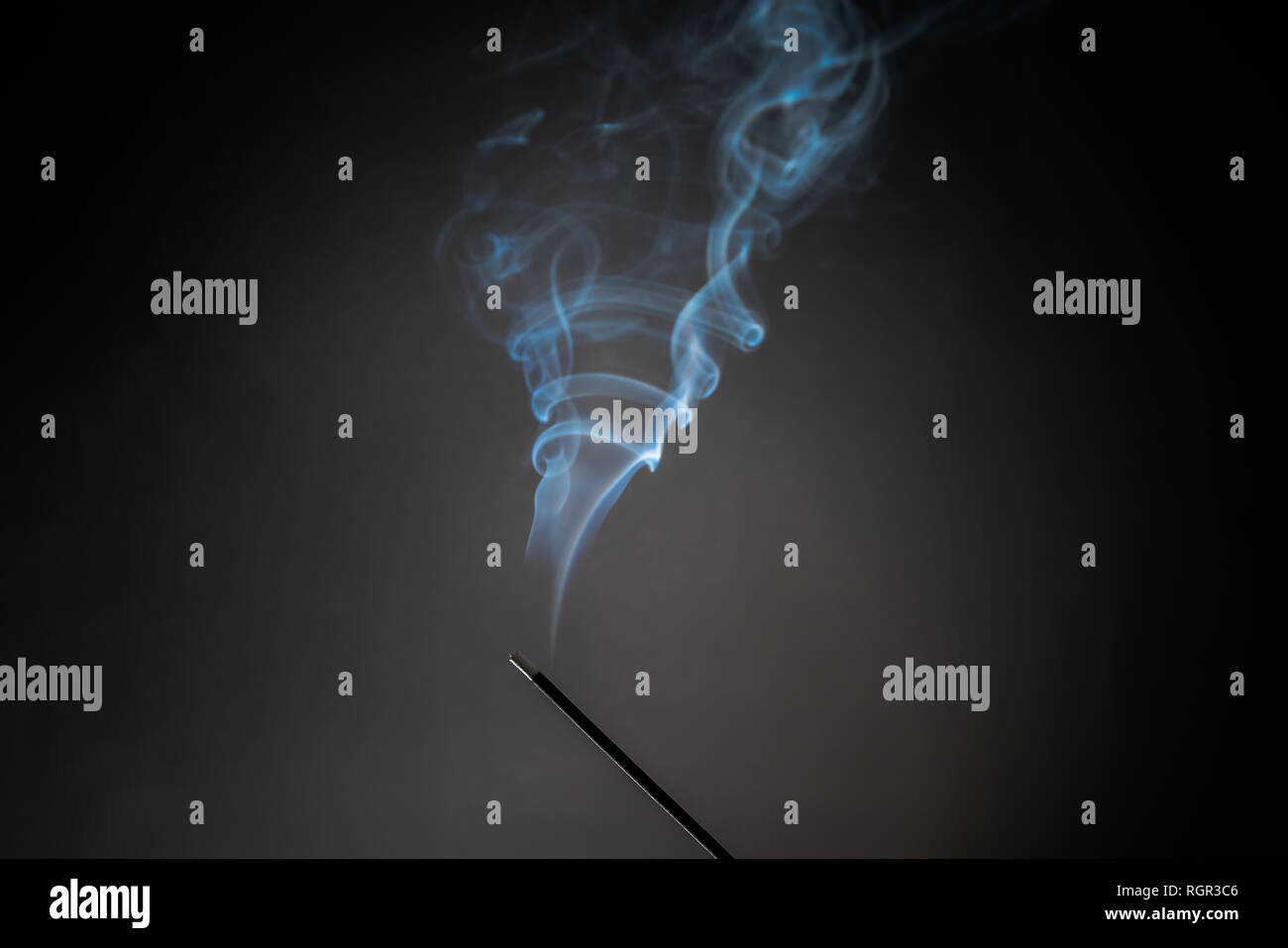 Smoking incense stick with smoke going up on Black Background. Pure