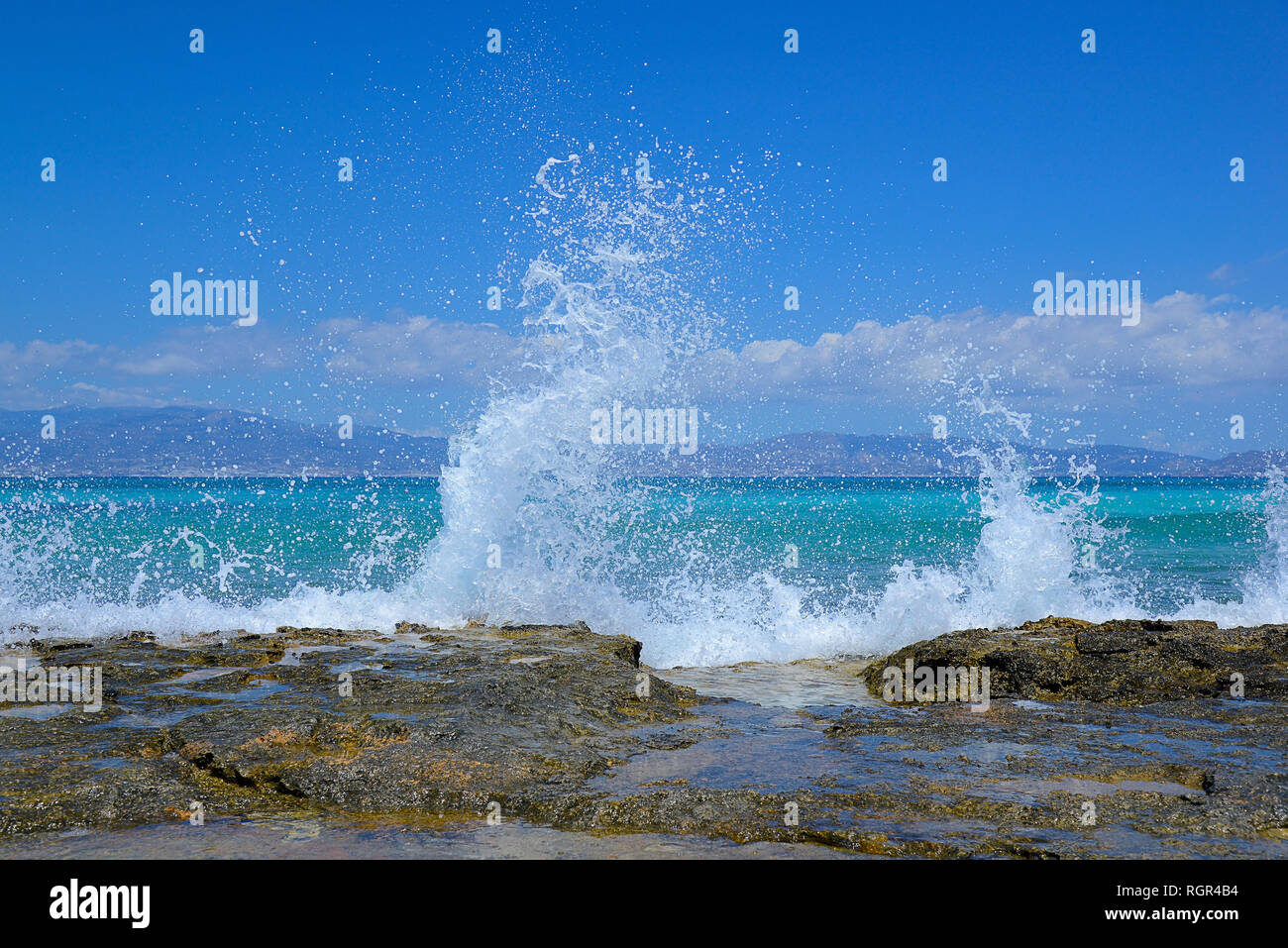 shore of large stone slabs, high splashing waves, blue sea, in the distance Crete island Stock Photo