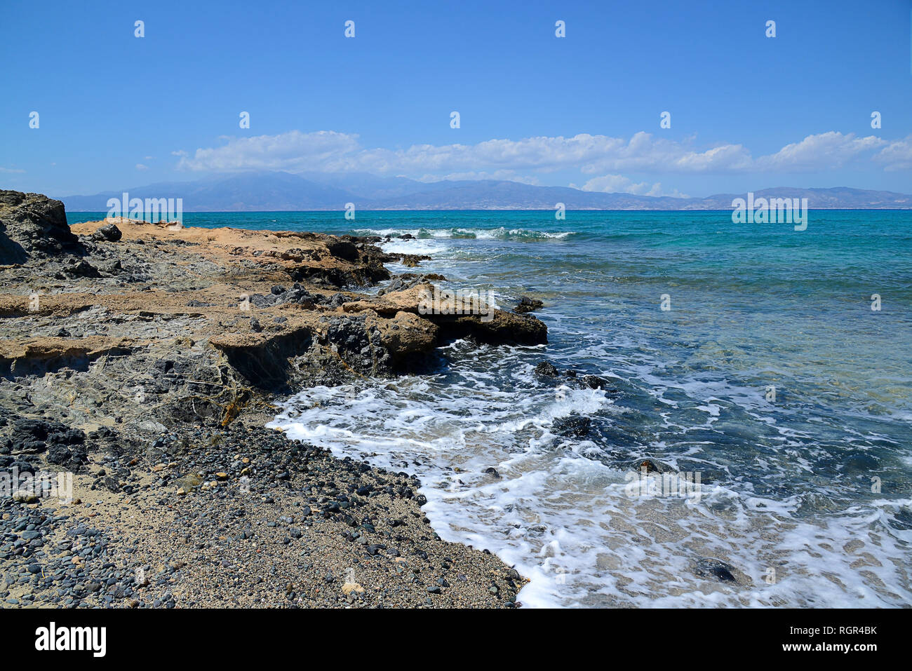 rocky shore, blue sea, mountains in the distance in the clouds Stock Photo