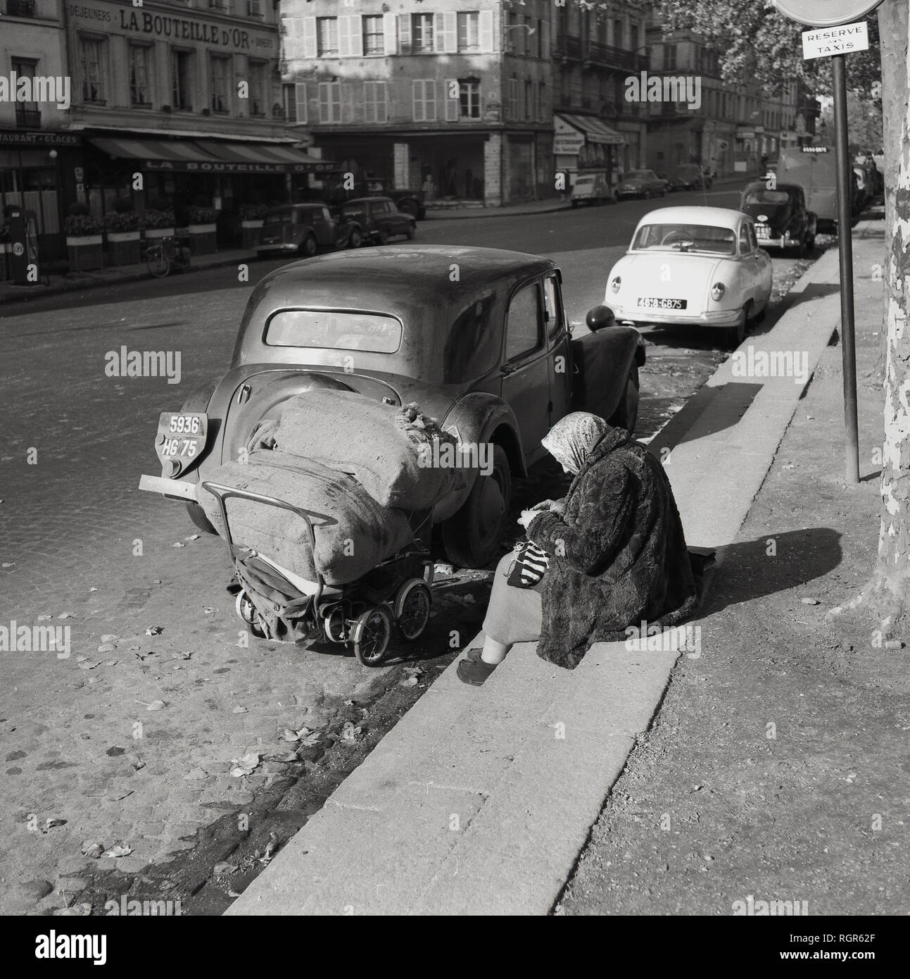 1950s, Paris, France, elderly lady, possibly a bag lady or vagabond,  wearing a fur coat sitting