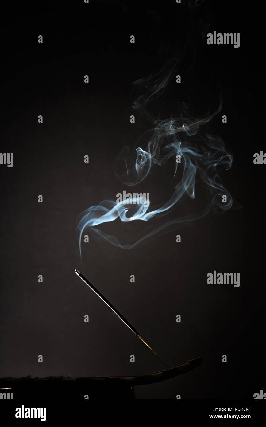 Smoking incense stick with smoke going up on Black Background. Pure