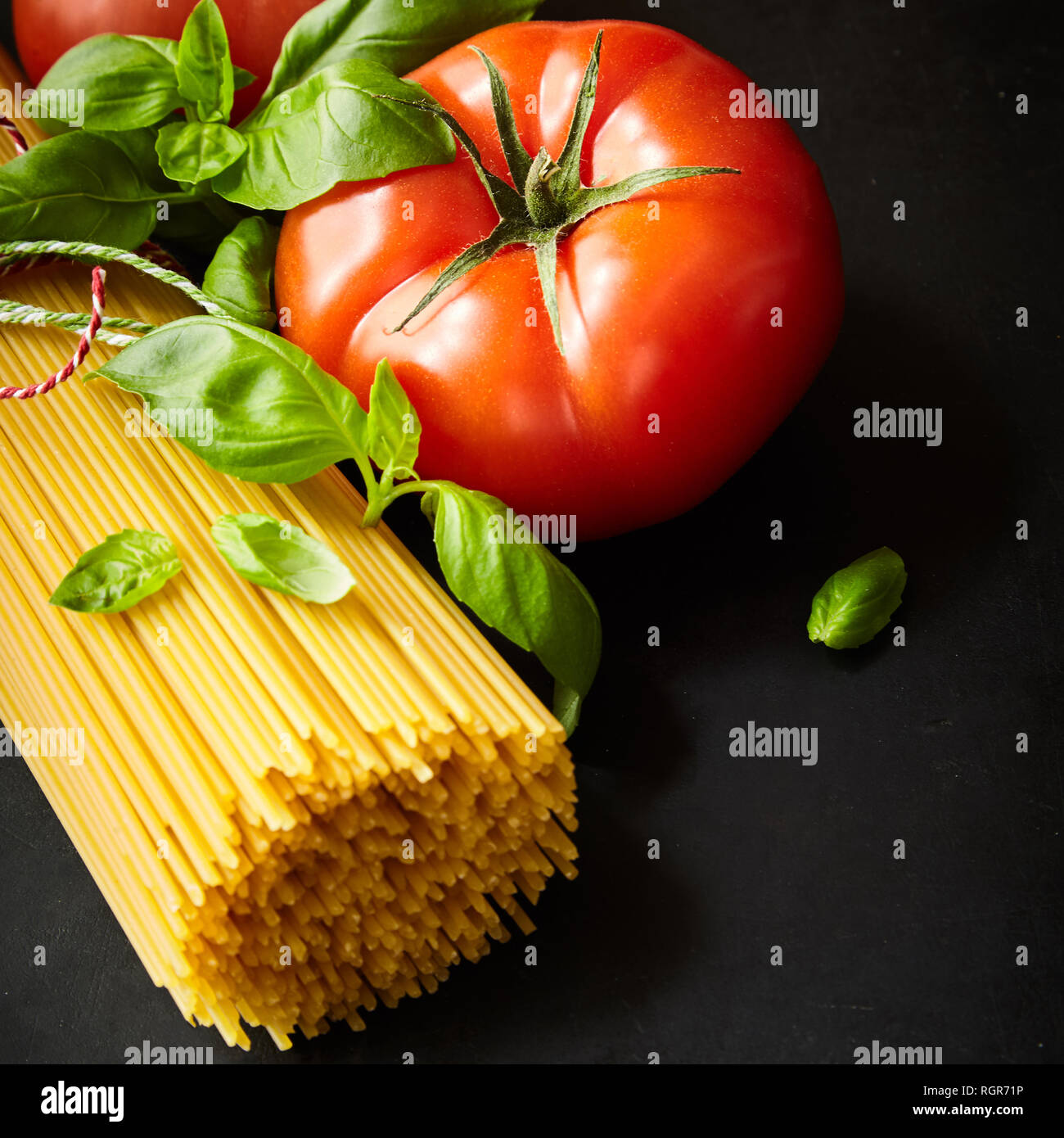 Bunch on spaghetti among tomato with fresh basil against dark background Stock Photo