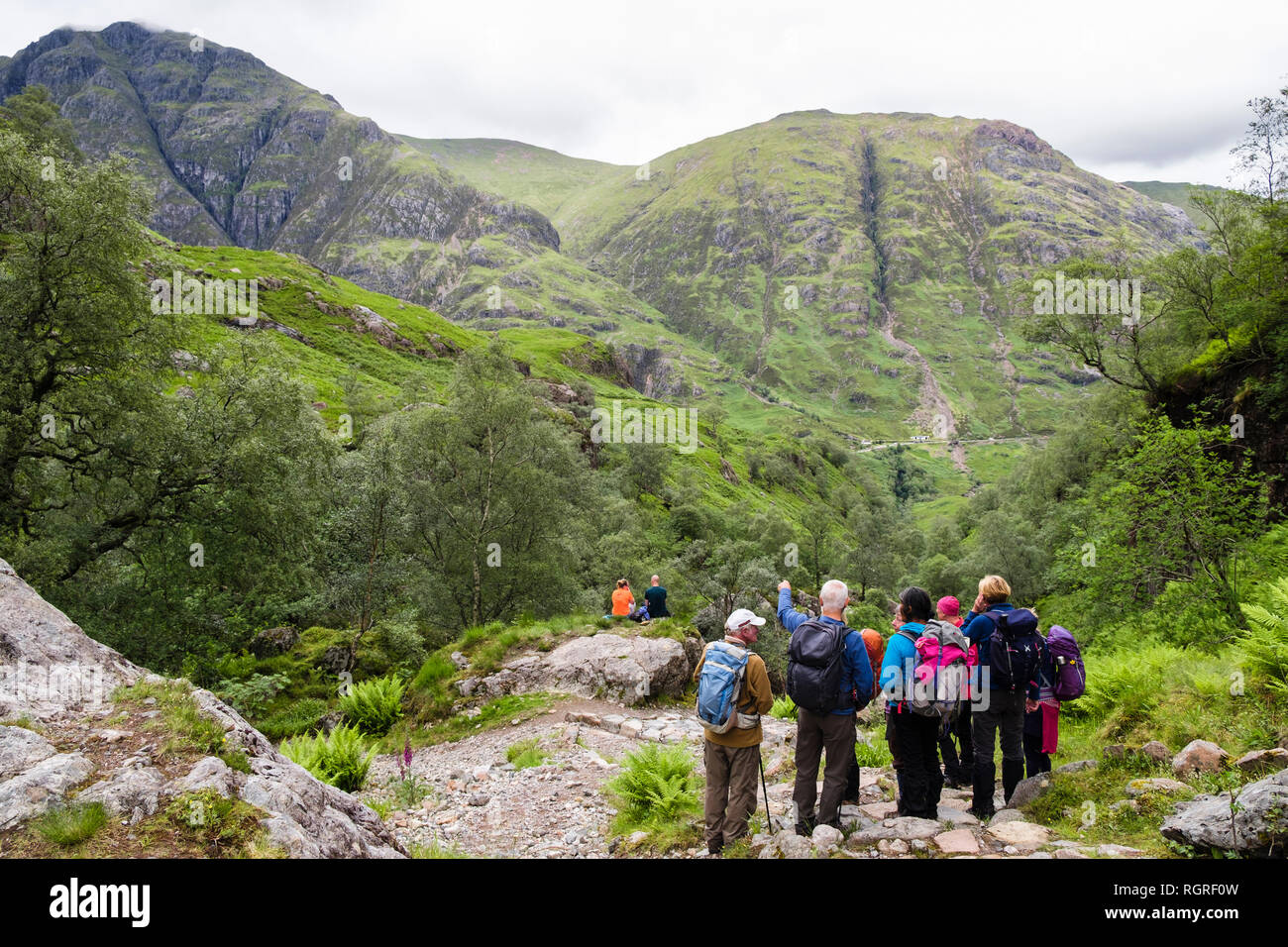 Group of hikers on path from the Lost Valley or Coire Gabhail looking at view to Am Bodach mountain across Glen Coe pass. Glencoe Highland Scotland UK Stock Photo