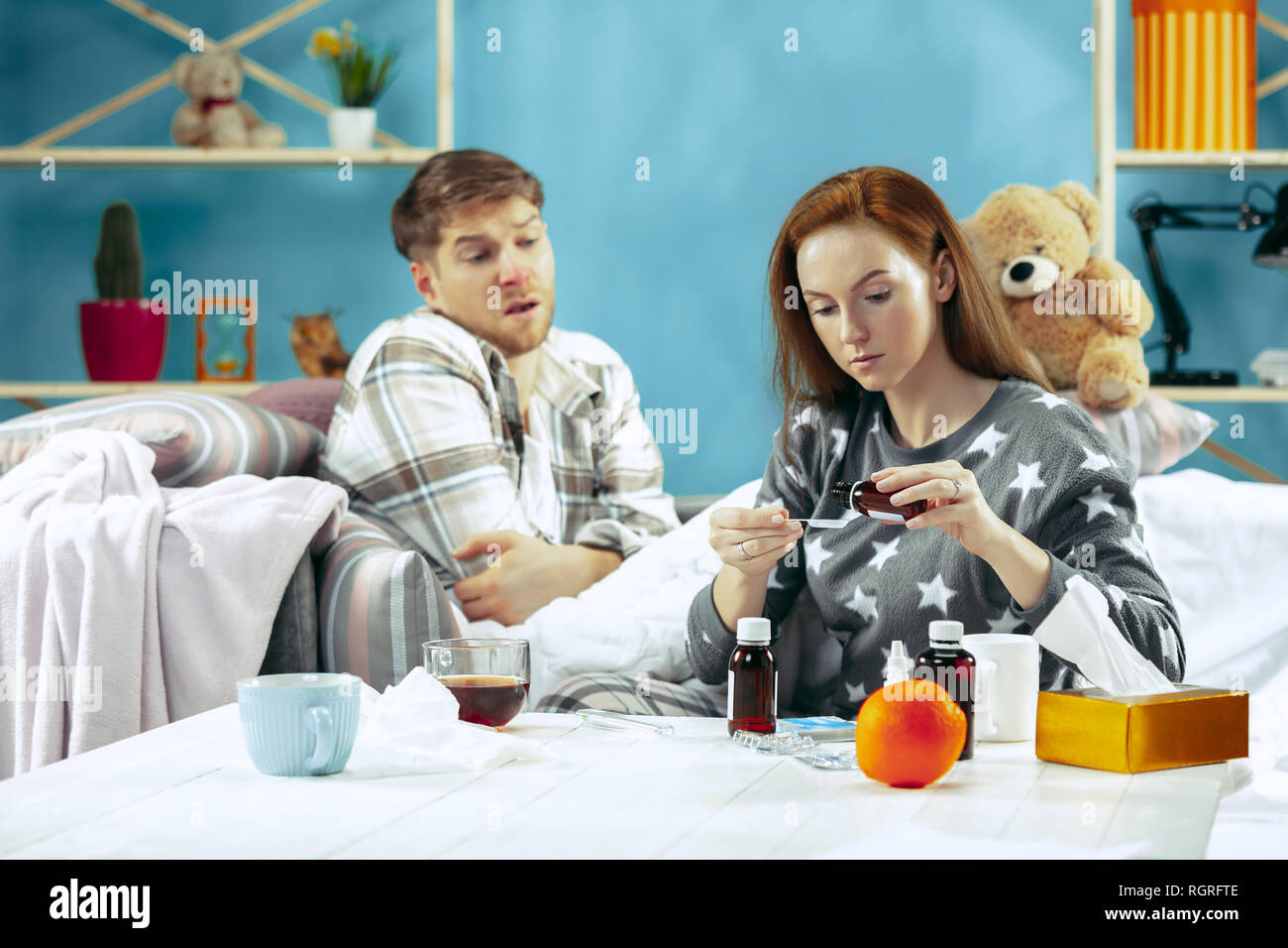 Sick man with fever lying in bed having temperature. The his wife take care for him. The illness, influenza, pain, family concept. Relaxation at Home. Healthcare Concepts. Stock Photo