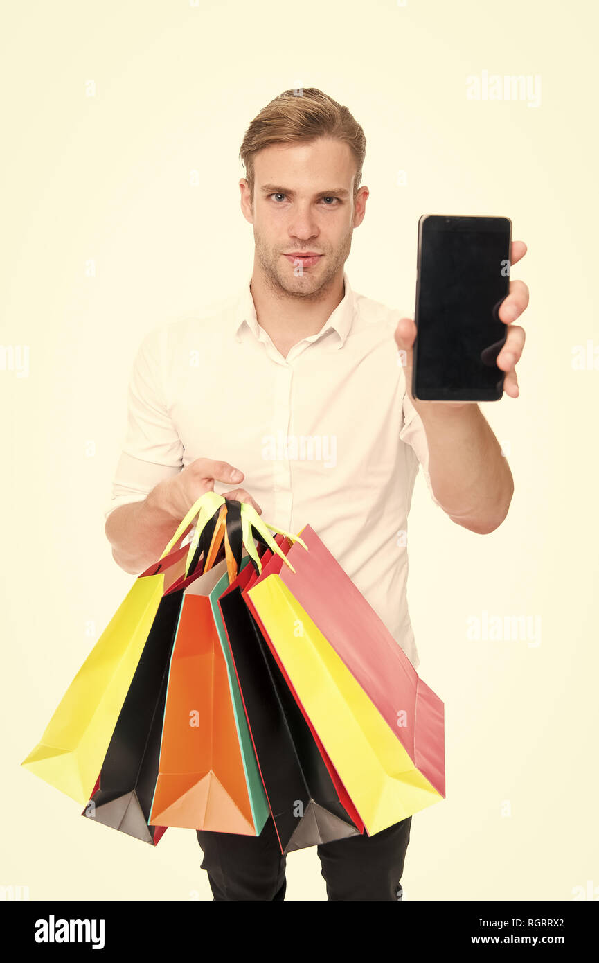 Guy buy fashionable clothes online with smartphone. Man happy client received packages purchases. Online shopping concept. Man takes advantages online shopping. Guy carries bunch colorful bags. Stock Photo