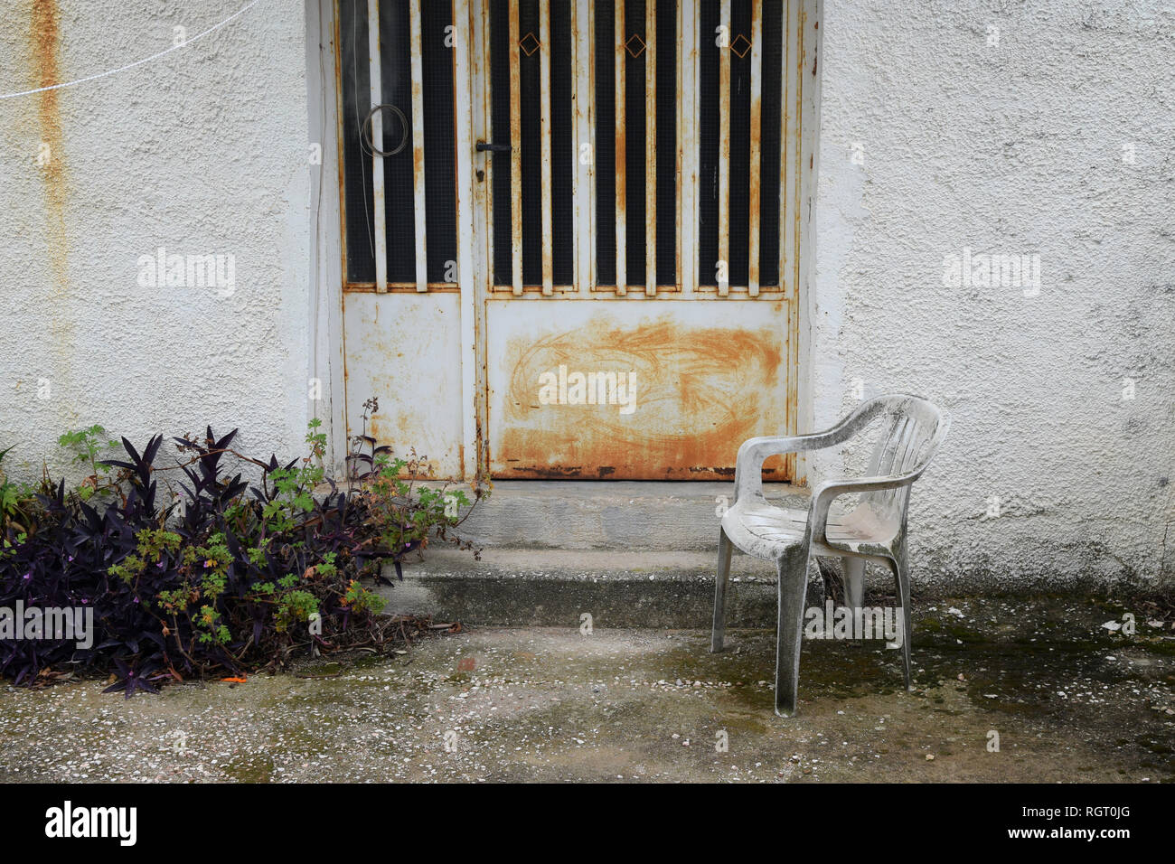 Plastic chair and rusty door. Abandoned house yard. Stock Photo
